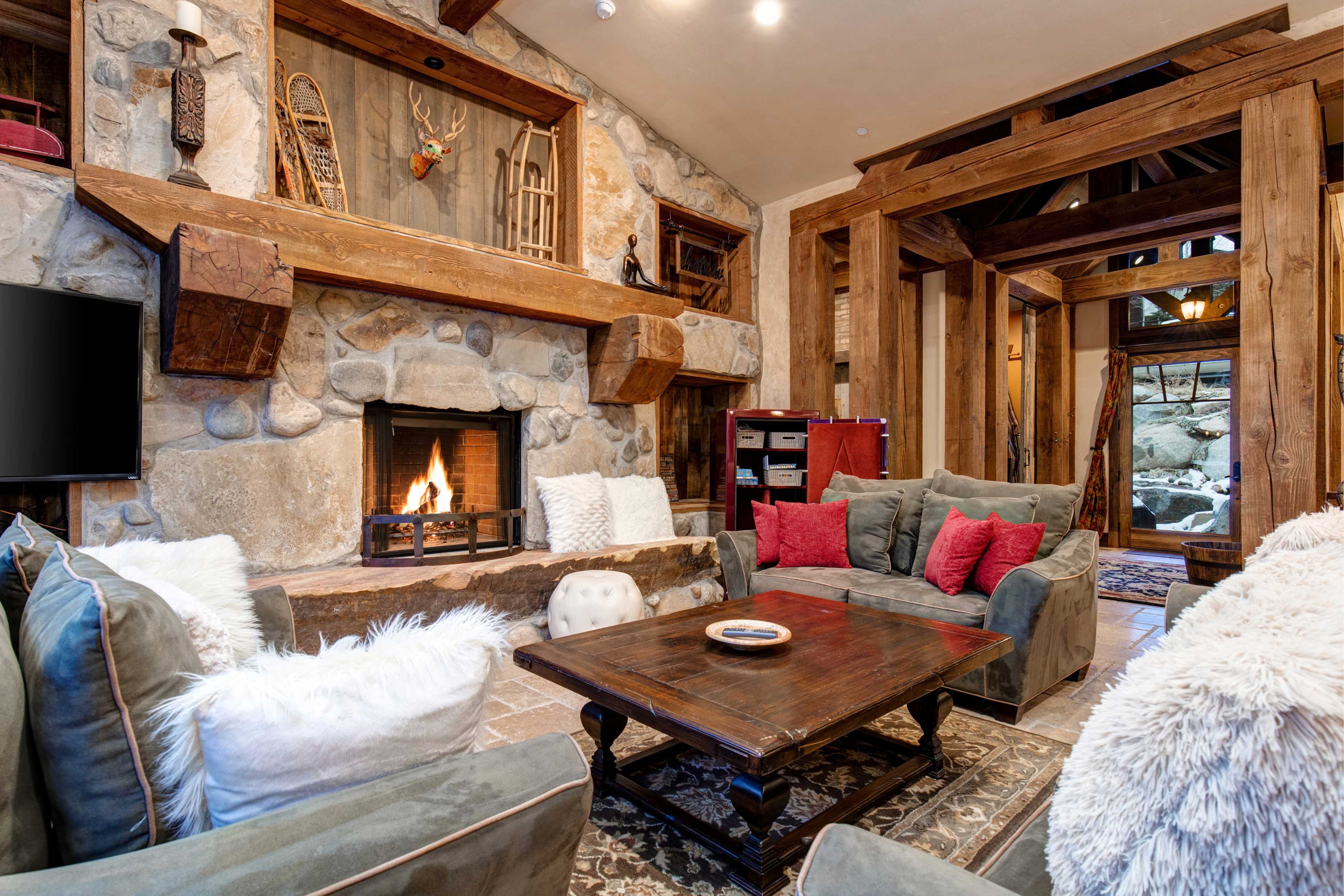 A cozy living room features a stone fireplace surrounded by comfortable seating and rustic wooden beams.