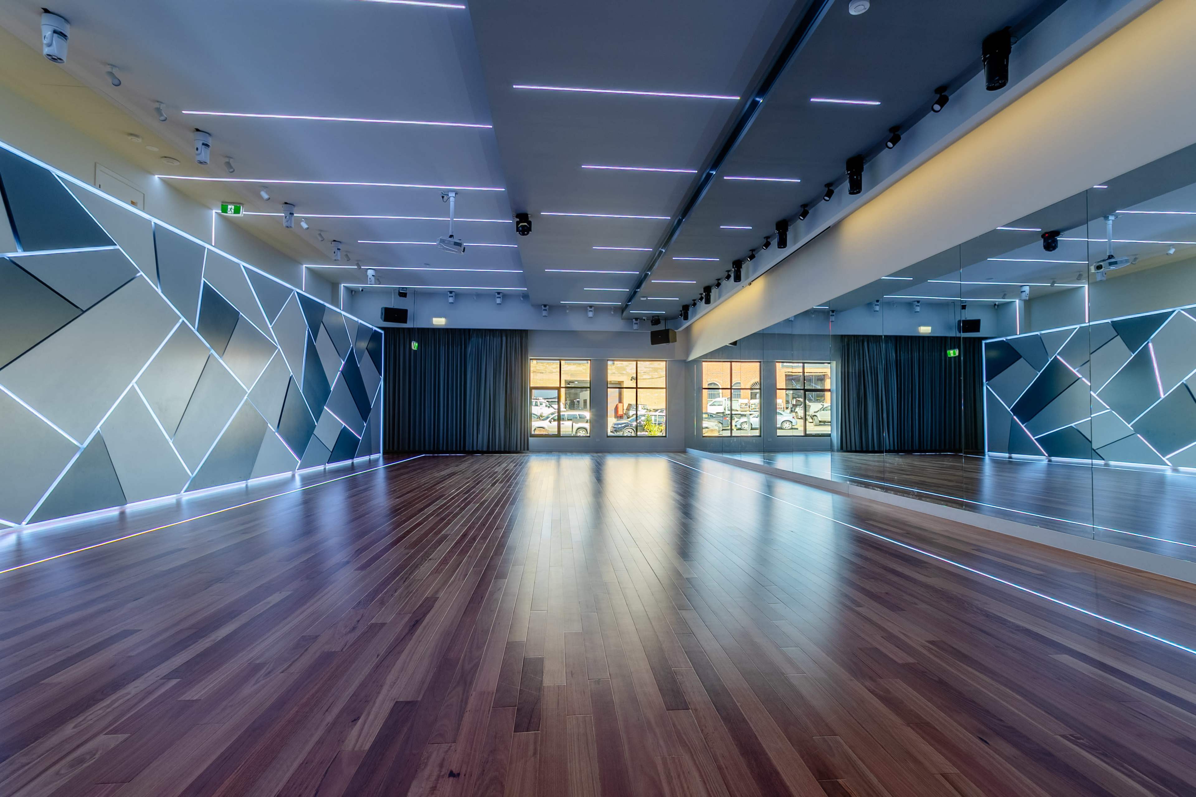 The image depicts a modern dance studio featuring polished wooden floors, large mirrors, and patterned wall panels with LED lighting.