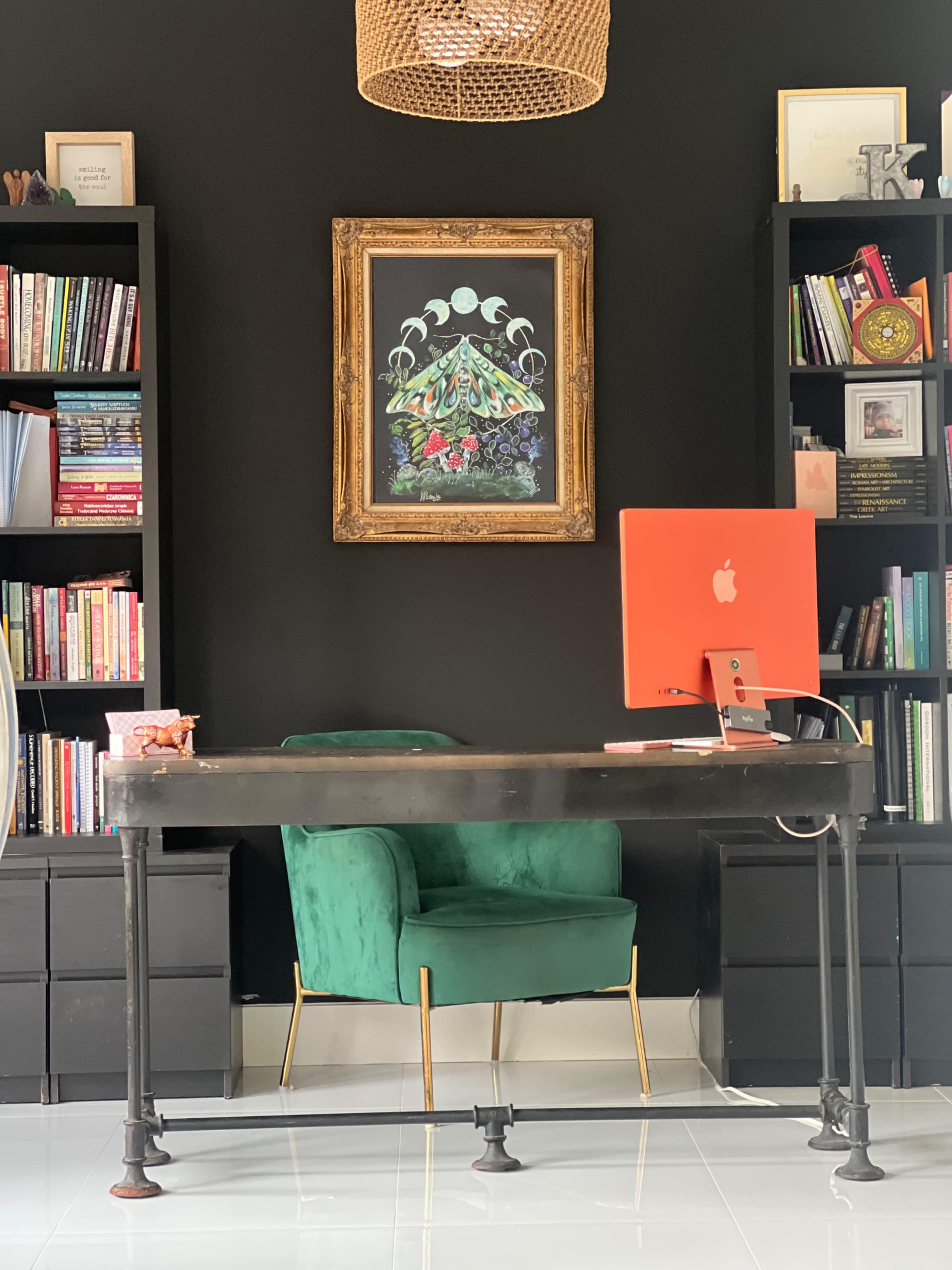 The image shows a modern office space featuring a black wall, a green chair, a wooden desk, an orange iMac, and shelves filled with books and decor.