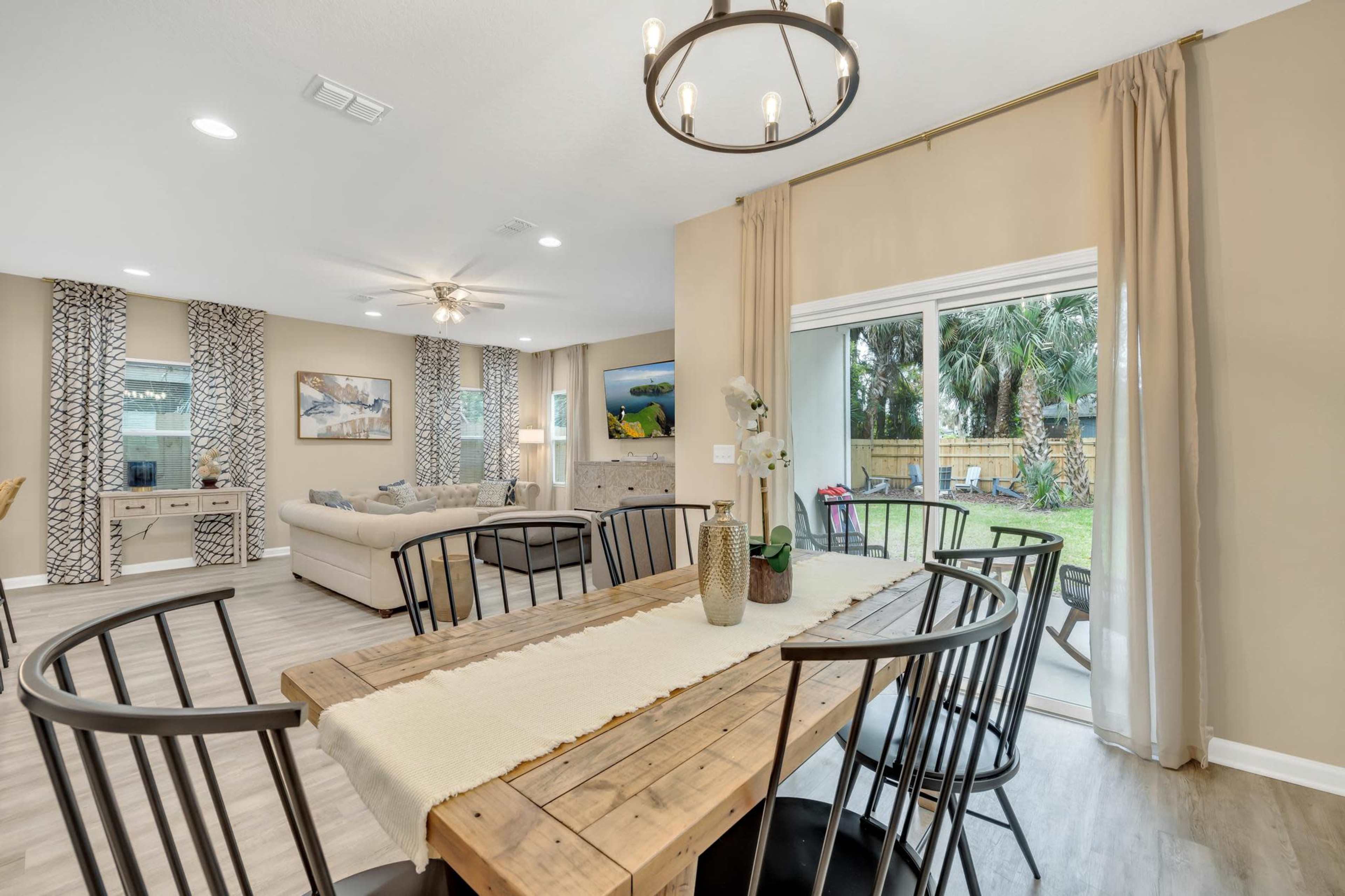 The image depicts a dining area with a wooden table surrounded by black chairs, overlooking a backyard through a glass sliding door.