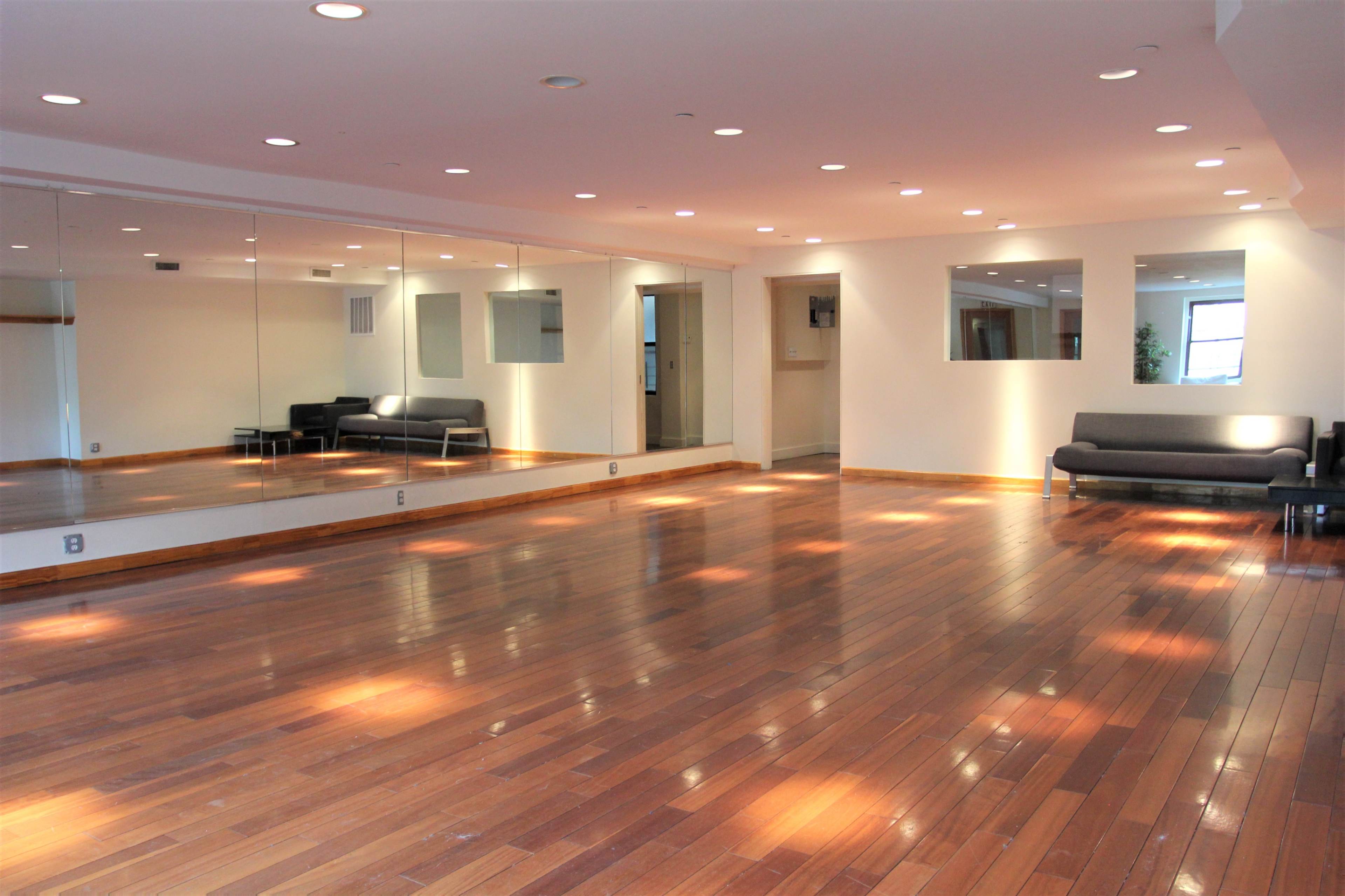 A spacious room with hardwood floors, large mirrors on one wall, and a gray sofa adjacent to the mirrored surface.