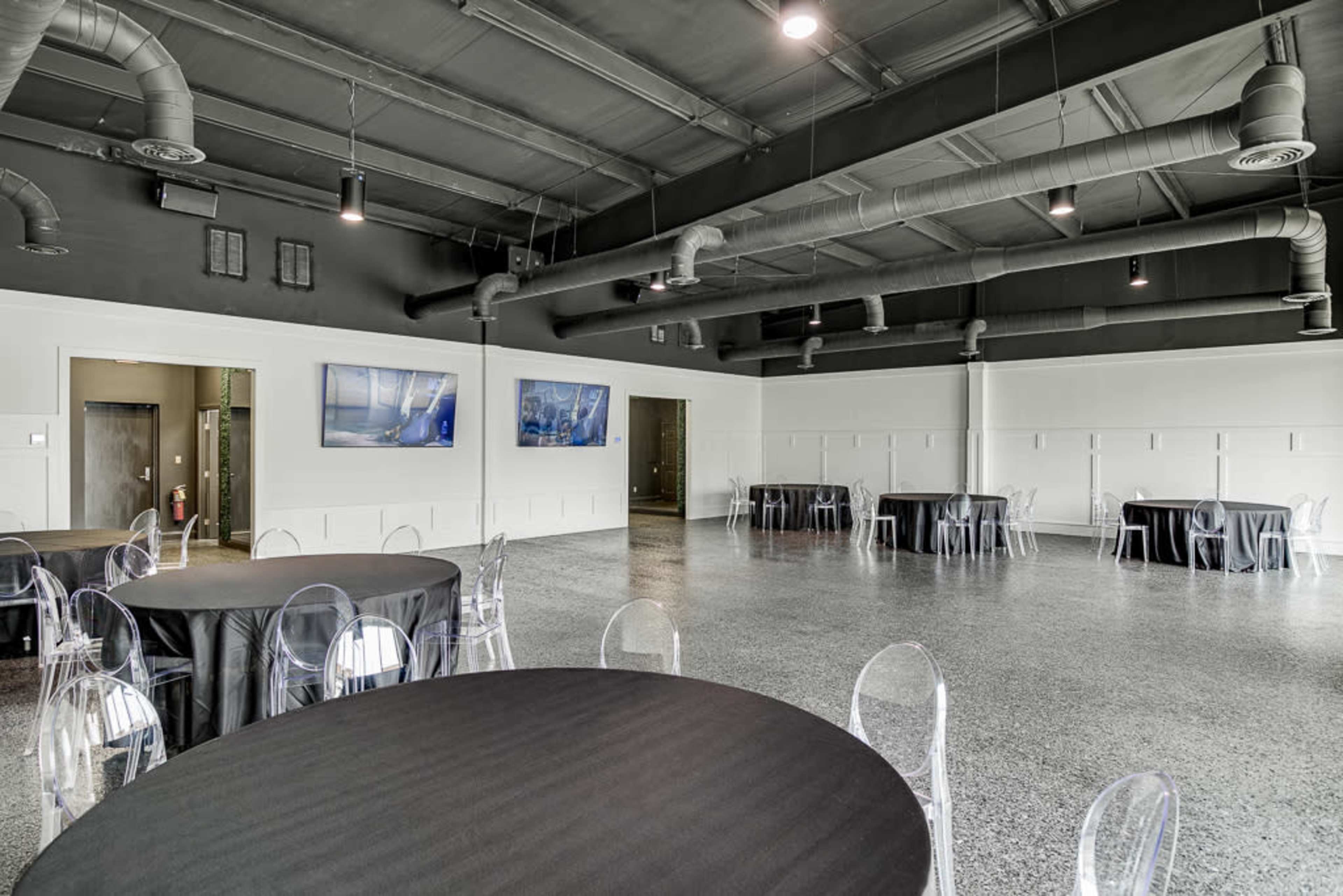 An empty event space with round tables covered in black tablecloths and modern wall art, featuring exposed ductwork on the ceiling.