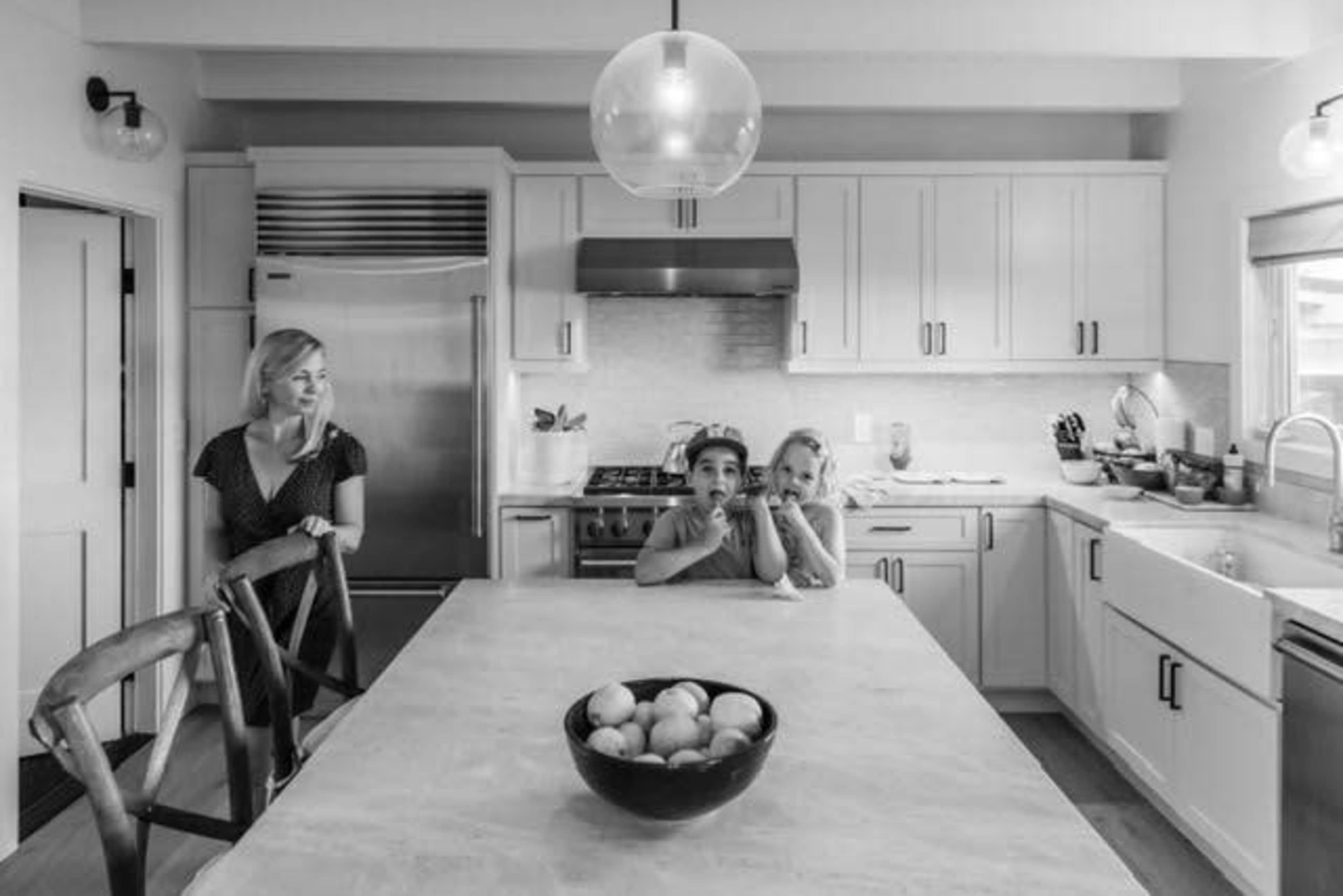 A woman and two children sit at a kitchen island while another woman stands nearby in a modern kitchen.