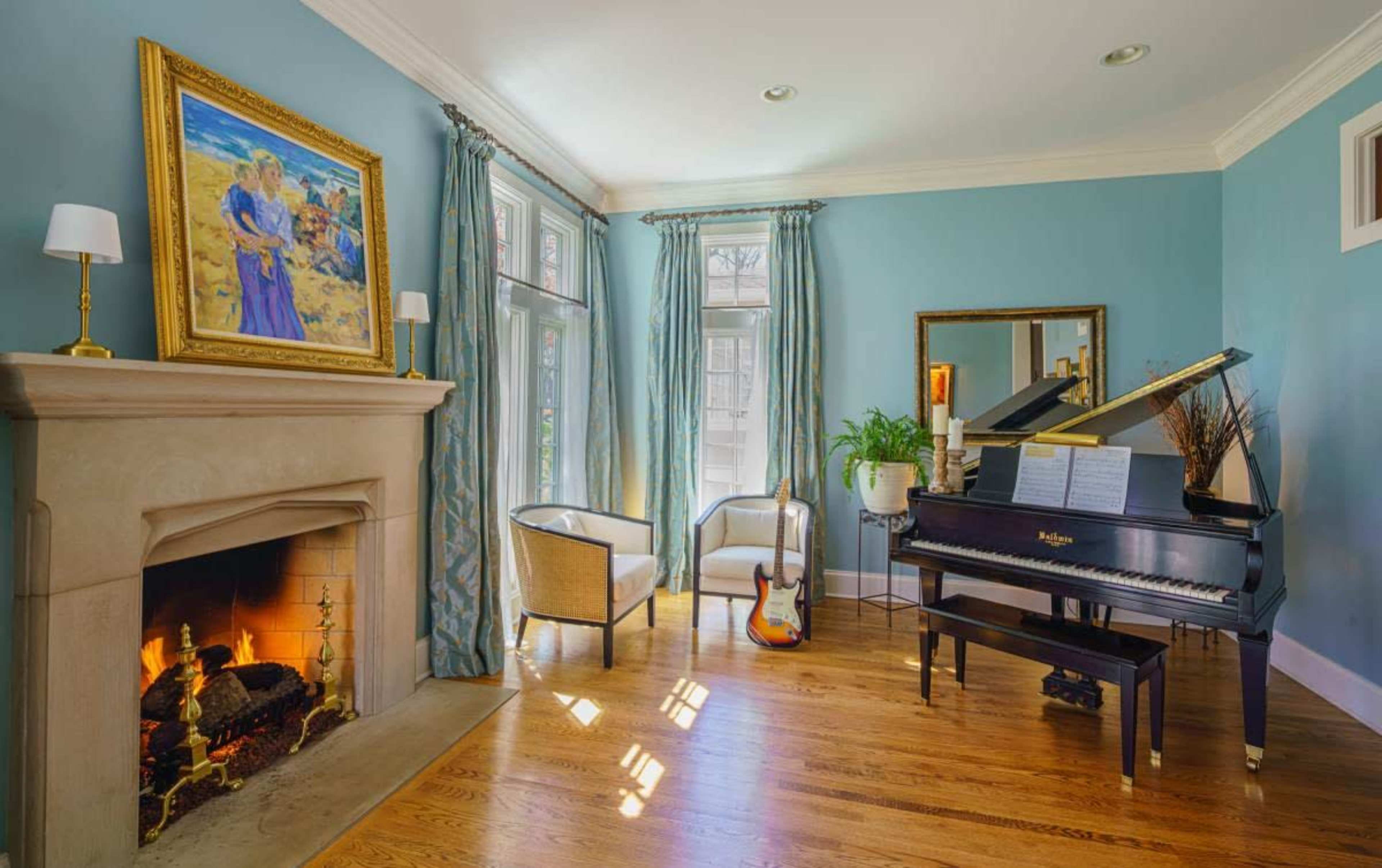 The image shows a cozy room featuring a grand piano next to a stone fireplace, along with a guitar and a framed painting on the wall.