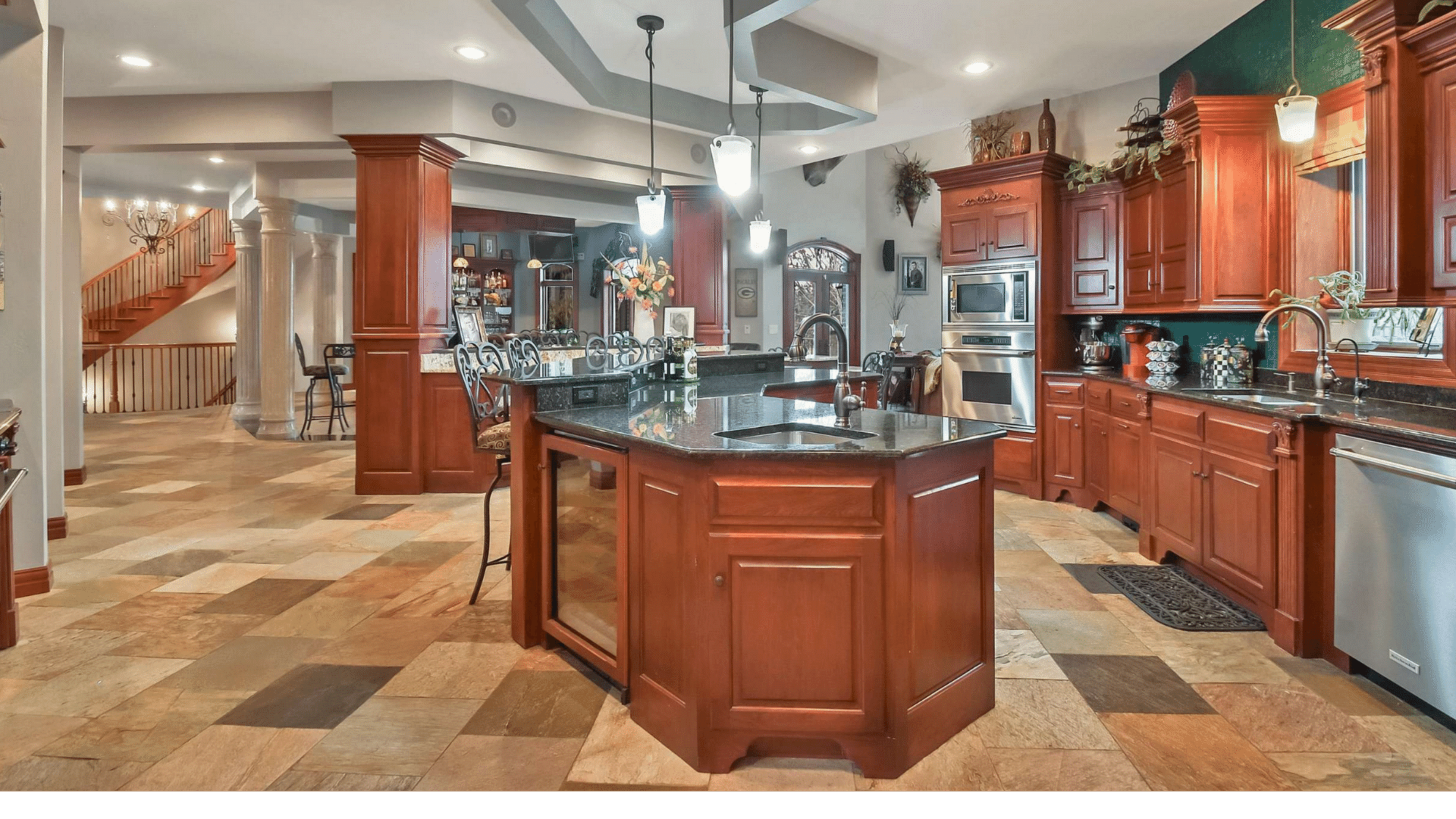 A spacious kitchen featuring dark wood cabinetry, a large central island with a black countertop, and a tiled floor.