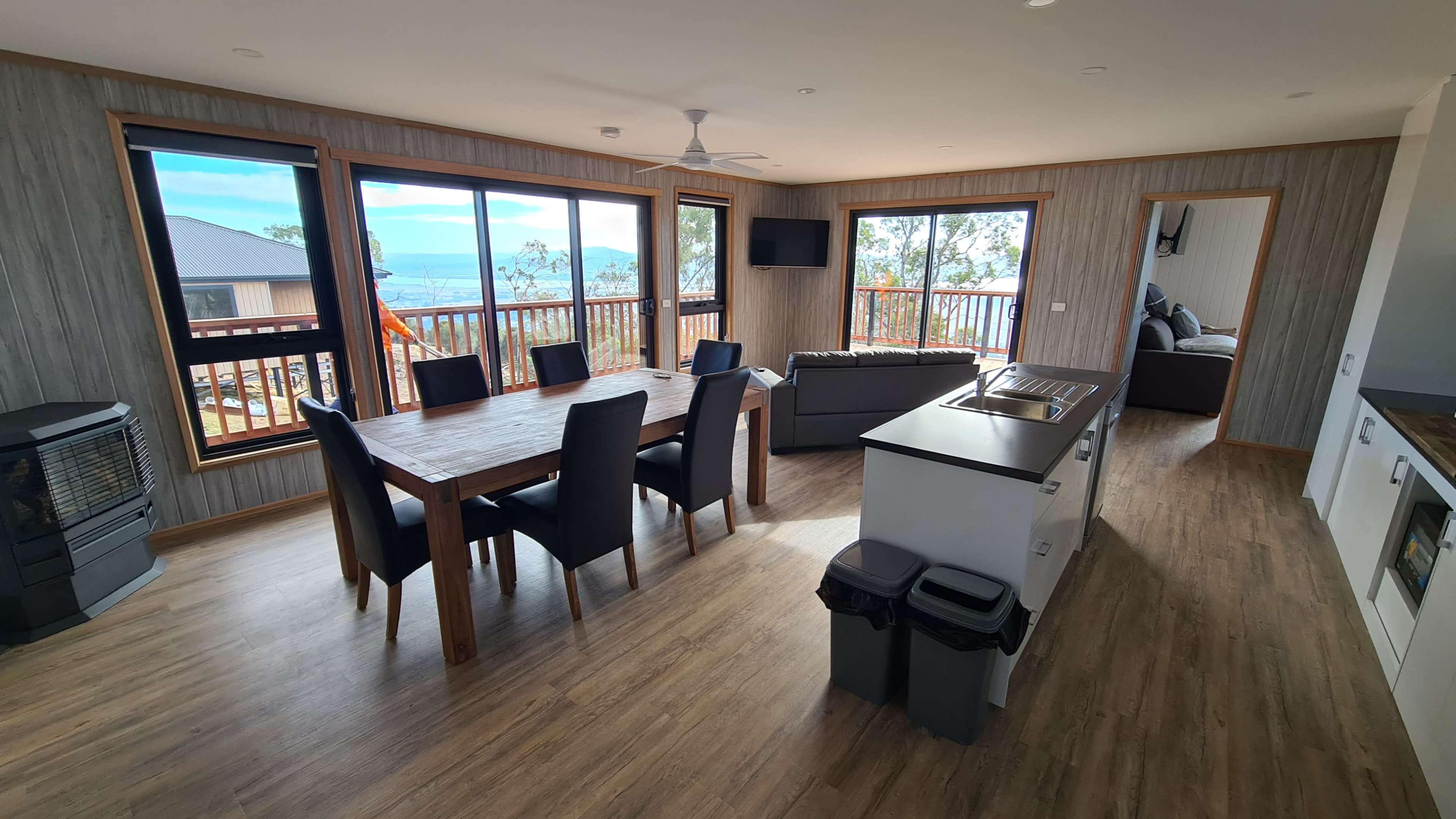 A modern open-concept living area with a dining table, kitchen, and large windows offering a view of the outdoors.