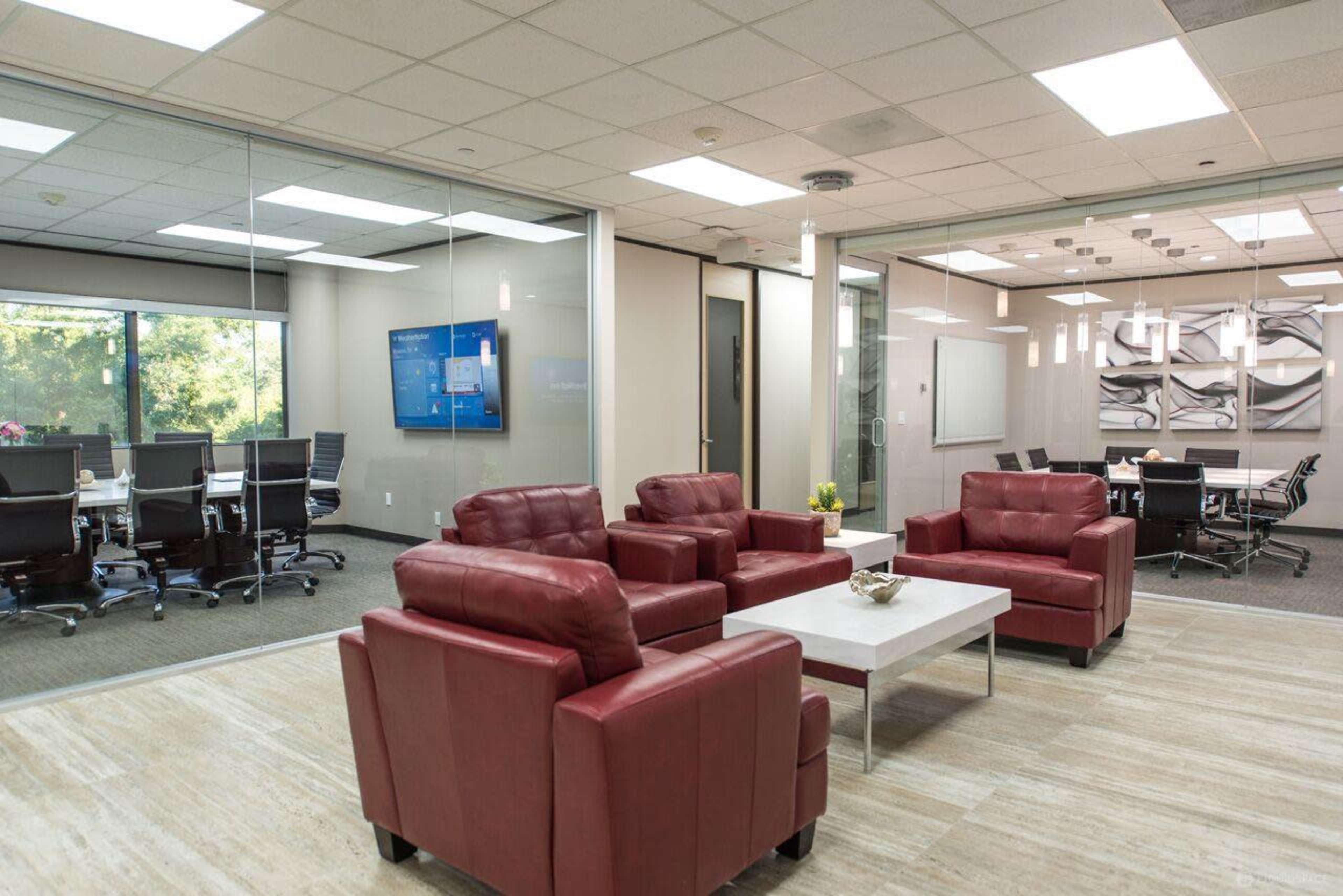 A modern office space with a seating area featuring red chairs, a coffee table, and a glass-walled conference room in the background.