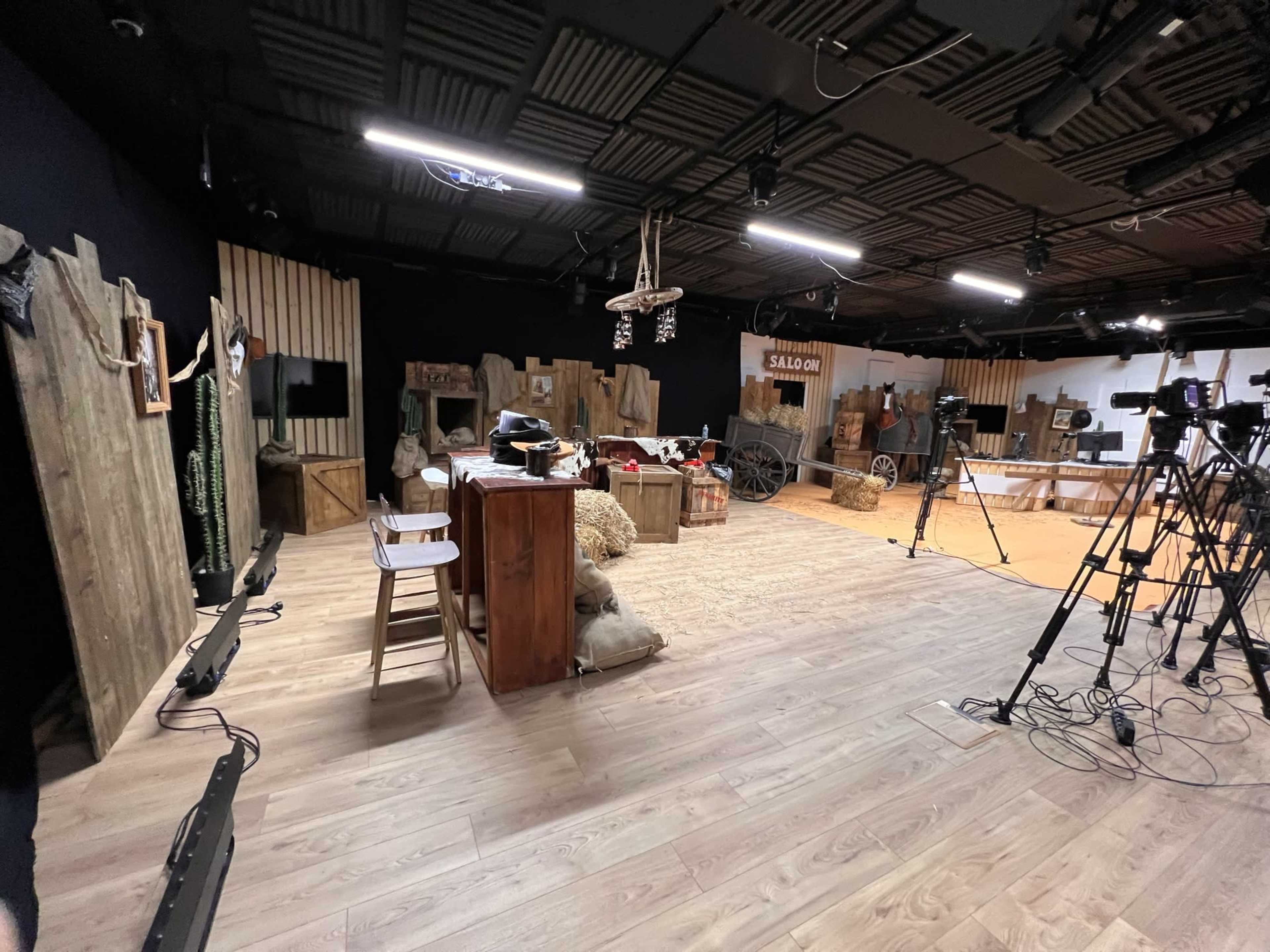 A studio setting designed to resemble a rustic environment, featuring wooden structures, camera equipment, and various props.
