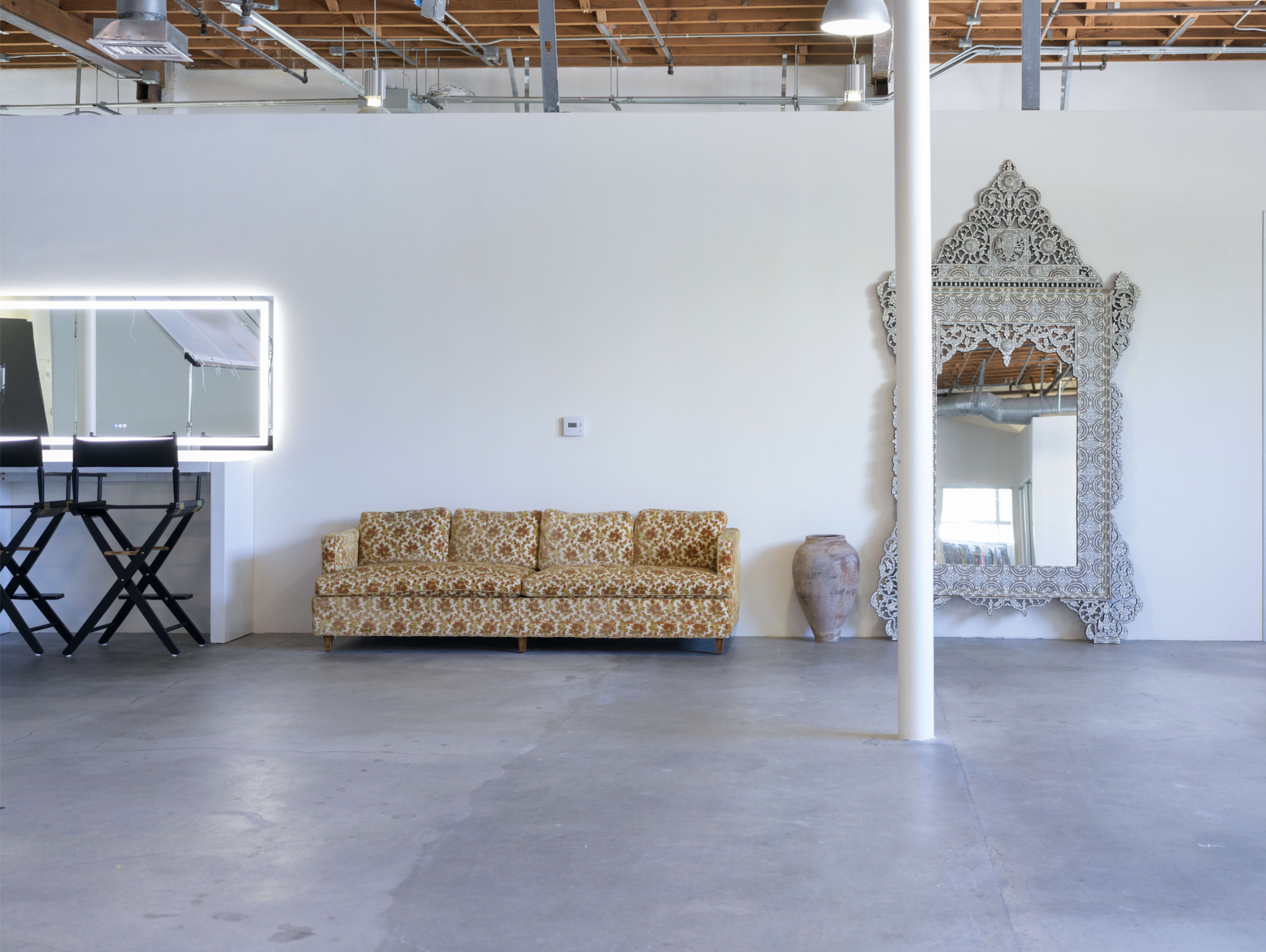 A spacious room with a patterned sofa, a large ornate mirror, a decorative vase, and a mirrored wall.