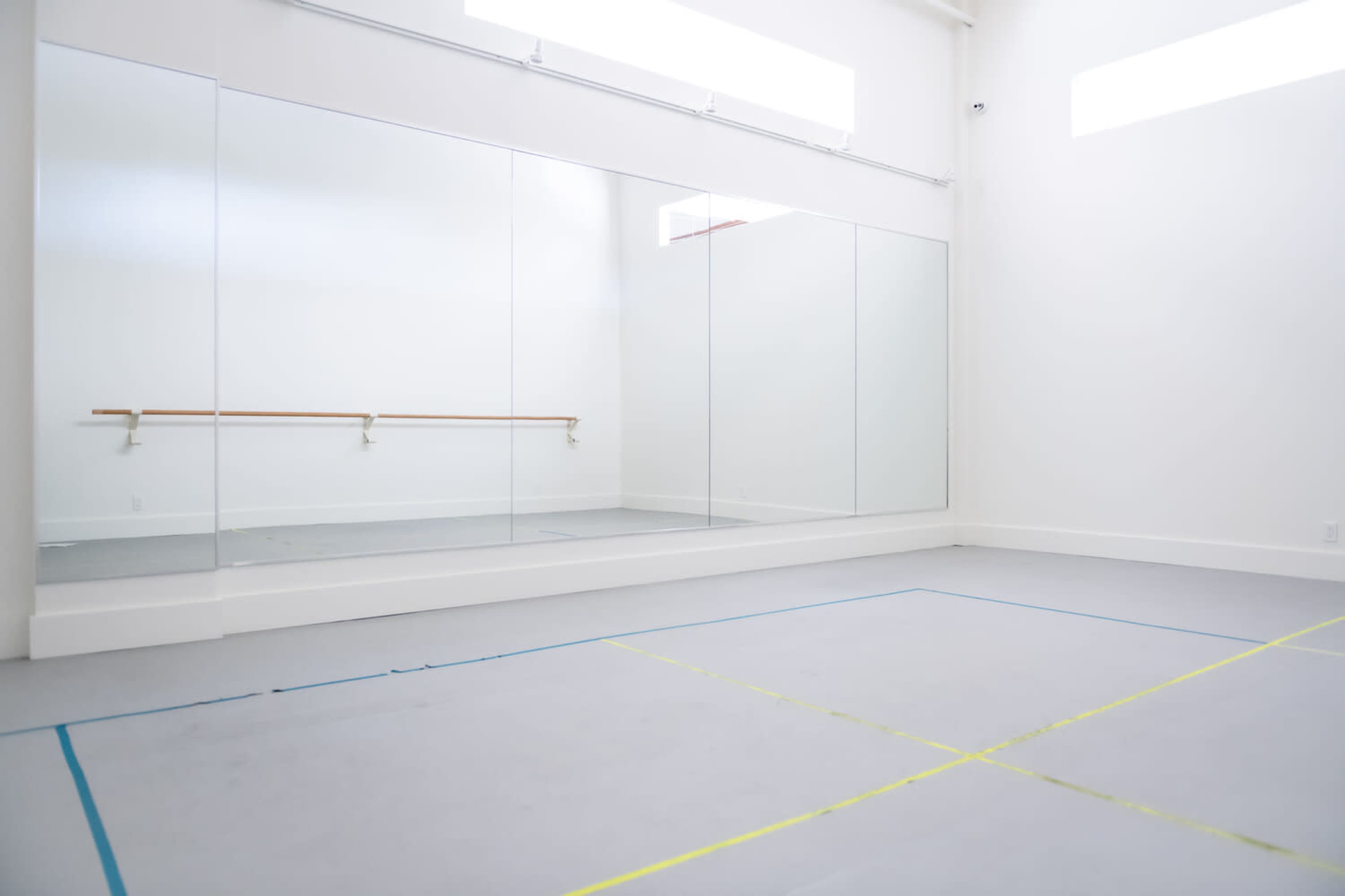 A spacious, brightly lit dance studio featuring large mirrors and a wooden barre along one wall.