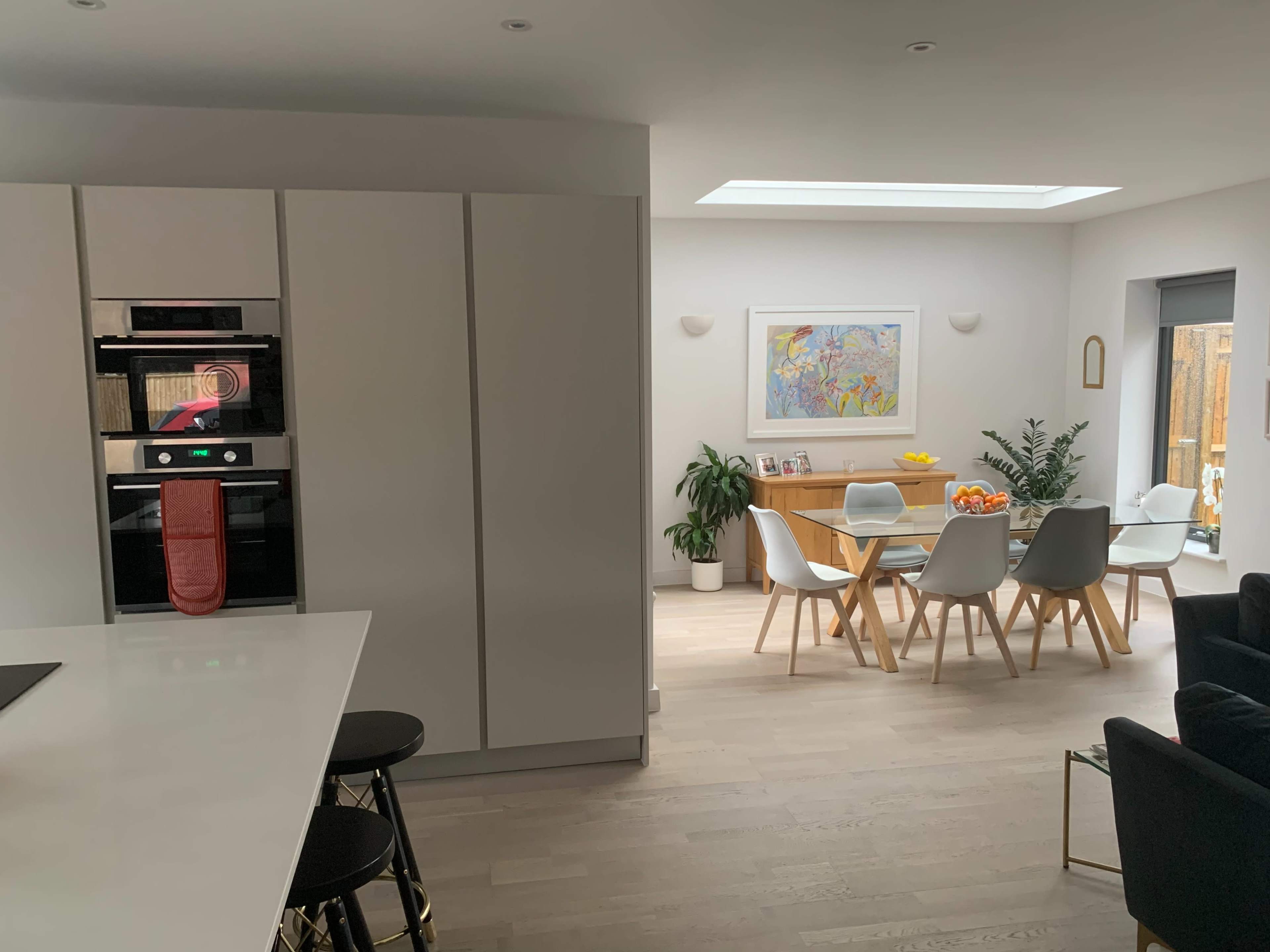 A modern kitchen area with white cabinetry, an oven, and a dining space featuring a wooden table and chairs filled with colorful fruit.