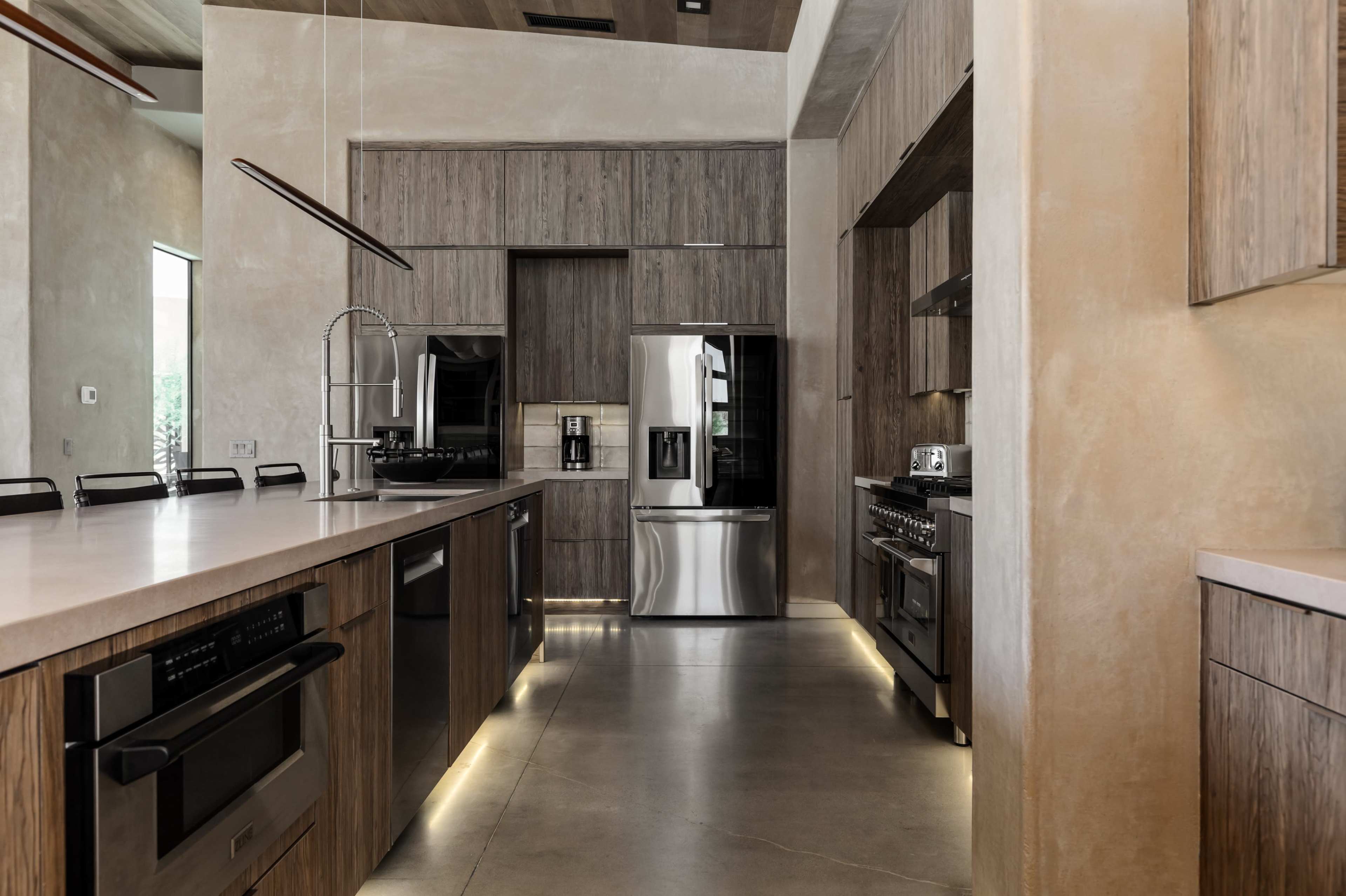 The modern kitchen features wooden cabinetry, stainless steel appliances, and a large central island with a minimalistic design.