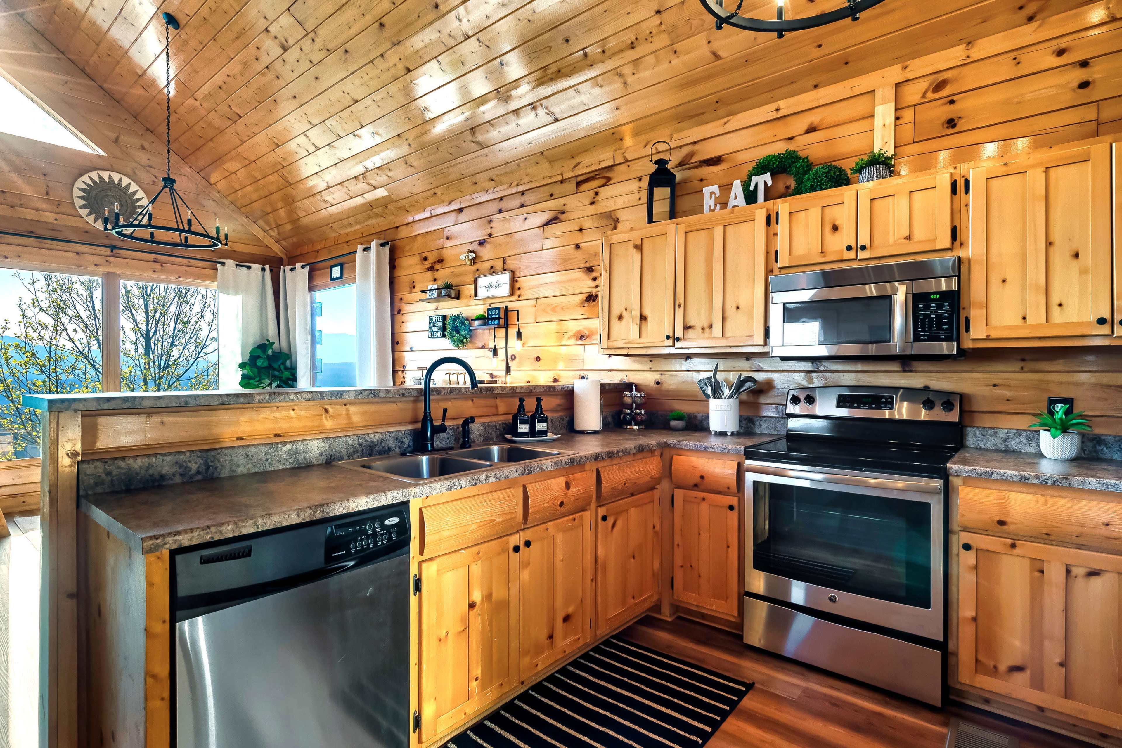 The image shows a wooden kitchen with a high ceiling, featuring stainless steel appliances, a stone countertop, and wooden cabinetry.