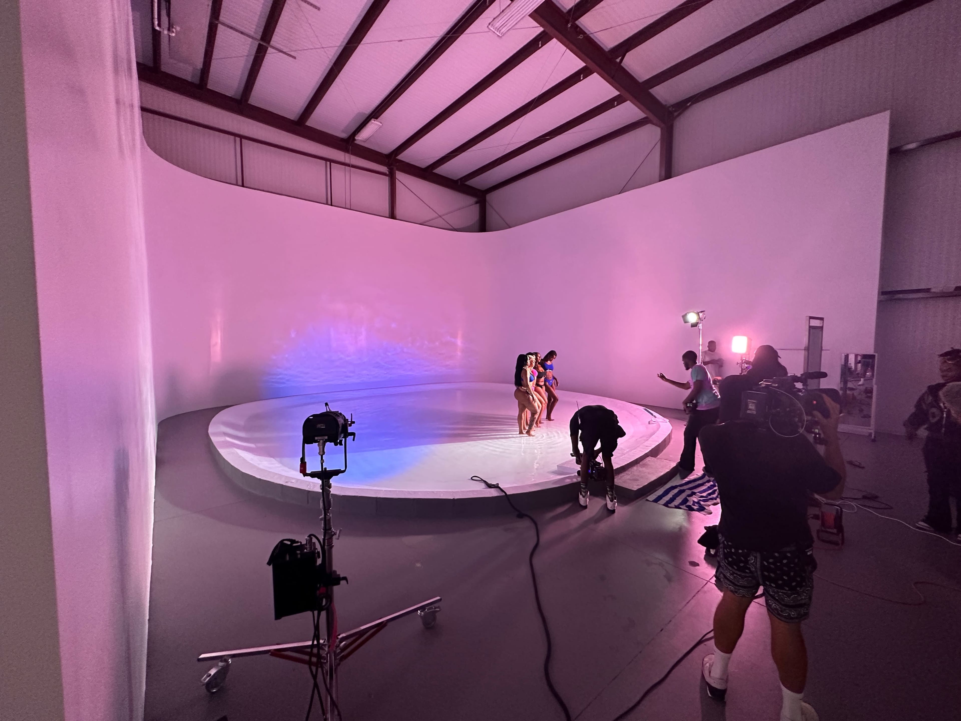 The image shows a filming setup in a large industrial space with a circular platform and multiple camera crew members preparing for a shoot.