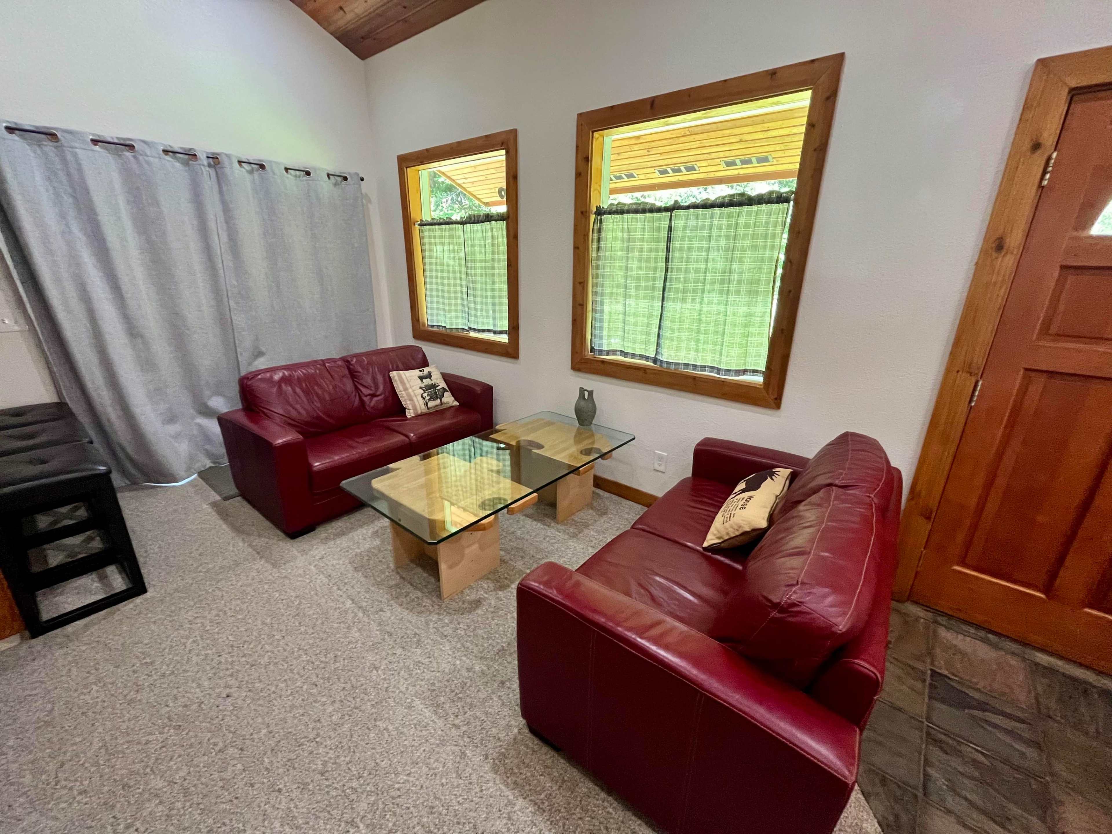 The scene shows a living room with two red leather sofas, a glass coffee table, and large windows with green curtains.
