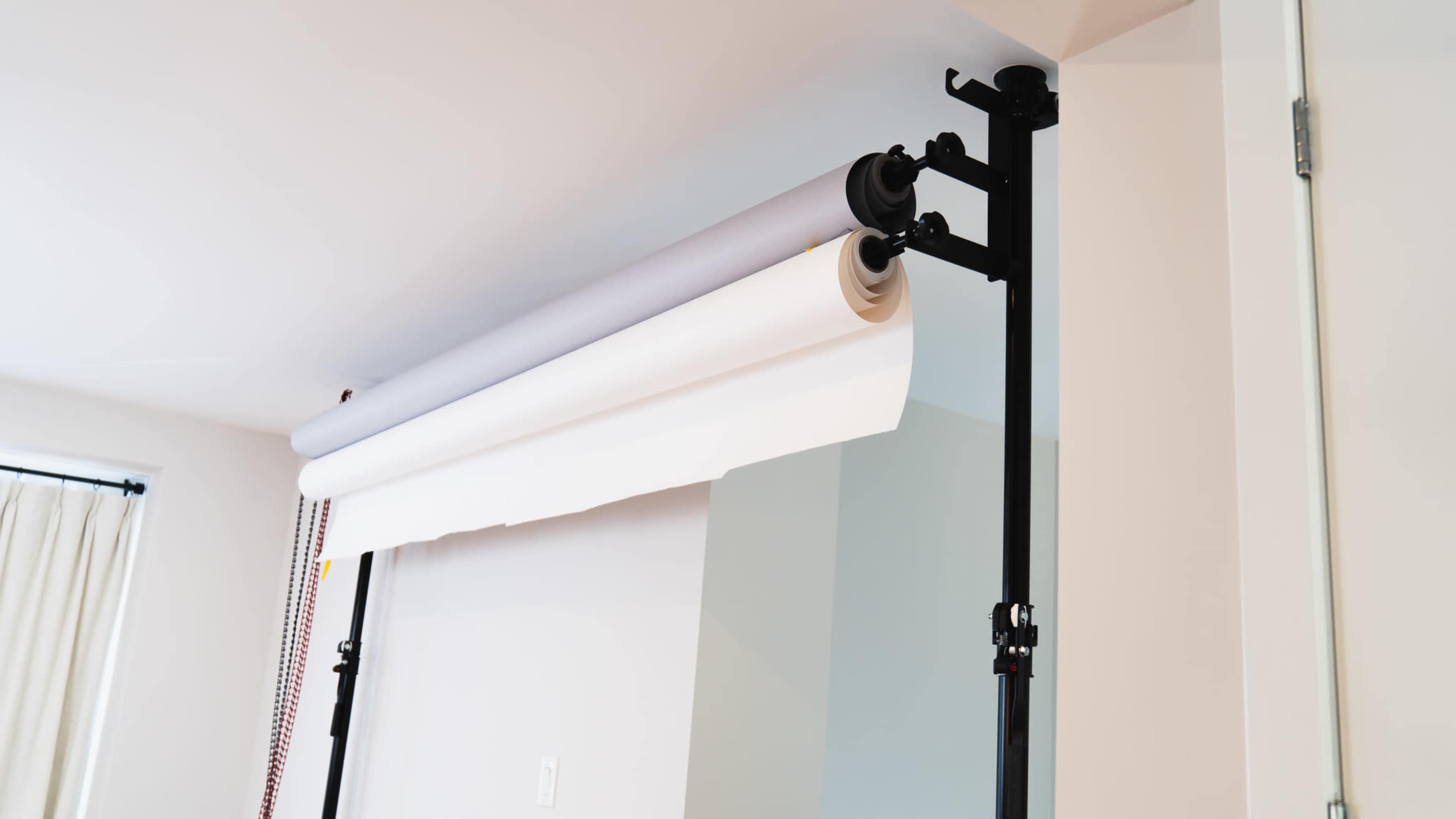 A photo backdrop system with a gray and white paper roll is mounted on a black support frame against a plain wall.