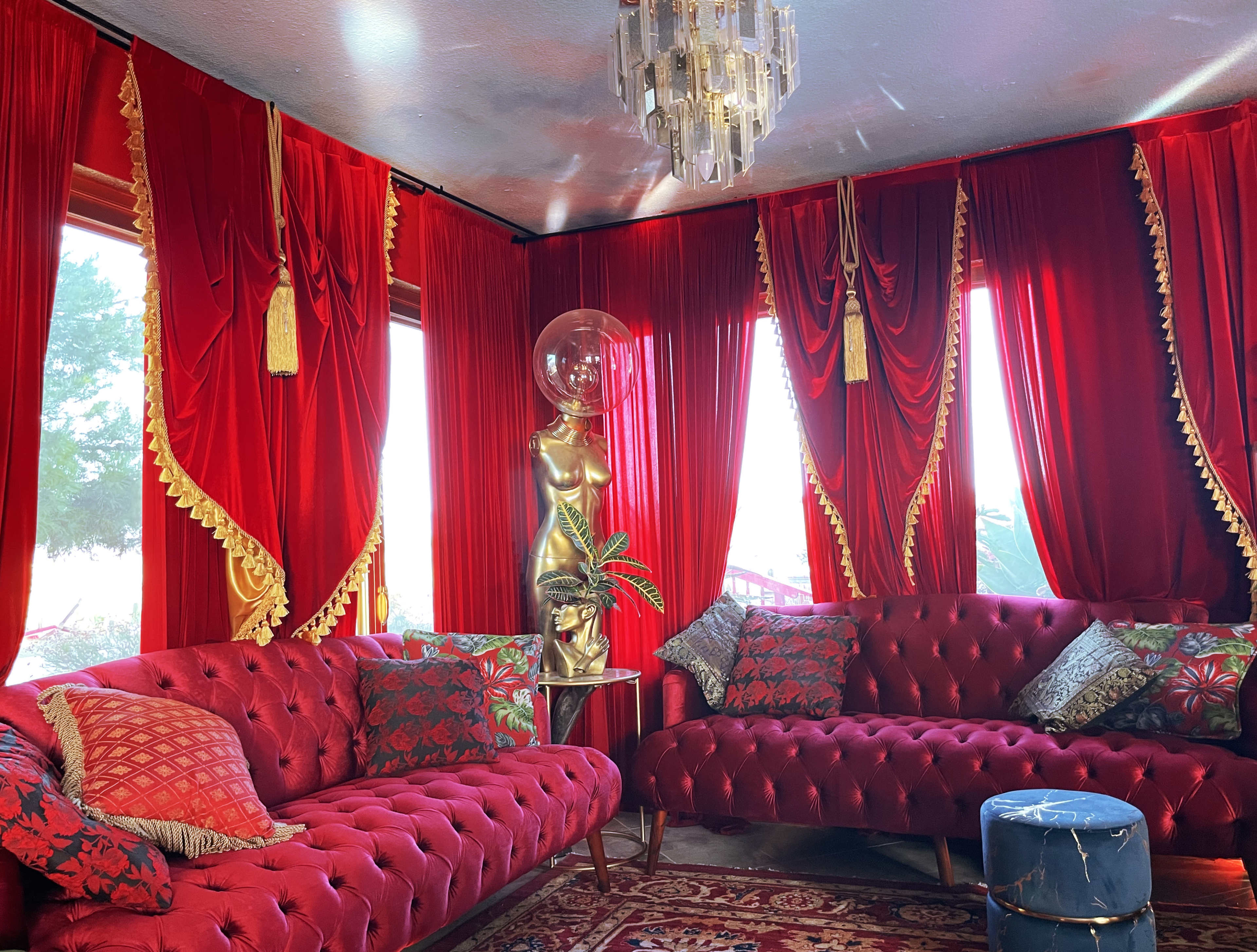 The room features plush red velvet sofas, gold accents, and large windows dressed with red drapes, creating an opulent atmosphere.