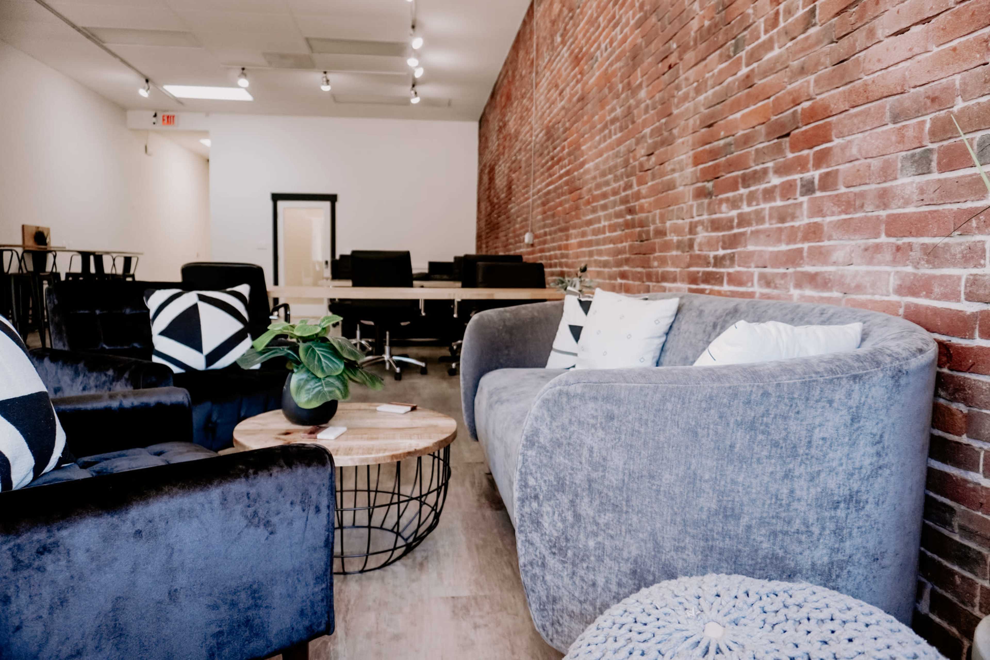 A modern interior with a brick wall, featuring black and white seating, a round wooden coffee table, and a few plants.