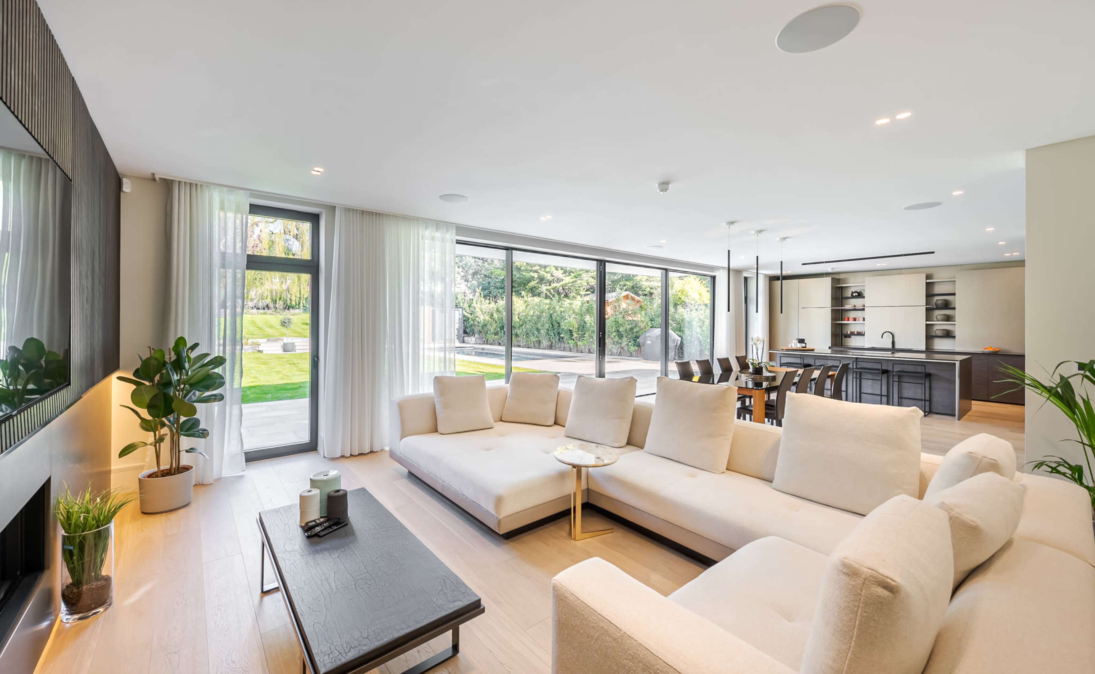 A spacious living room with a large light-colored sofa, a coffee table, and large windows that overlook a landscaped garden.
