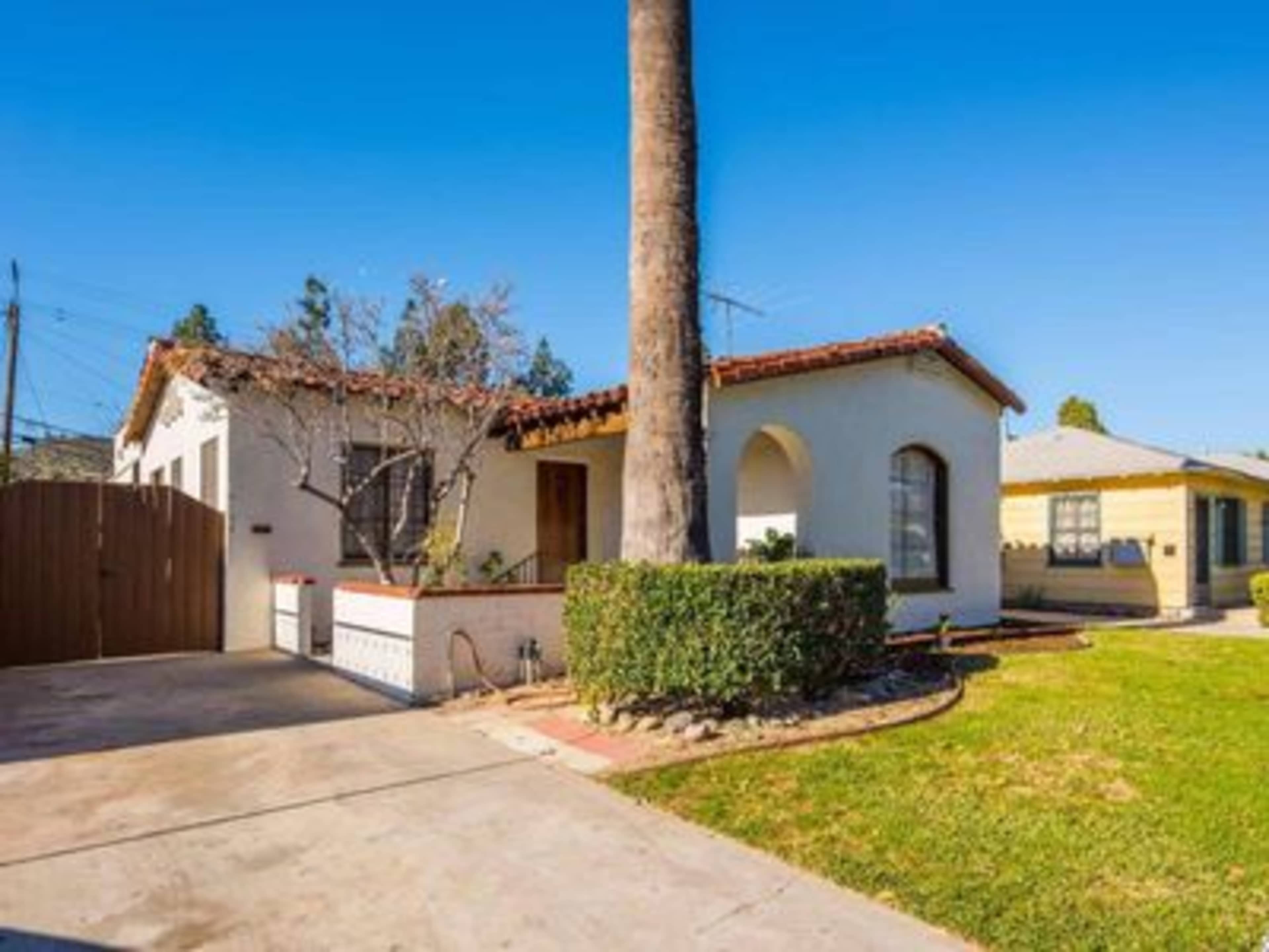 A single-story house with a palm tree in the front yard features a Spanish-style architecture and a concrete driveway.
