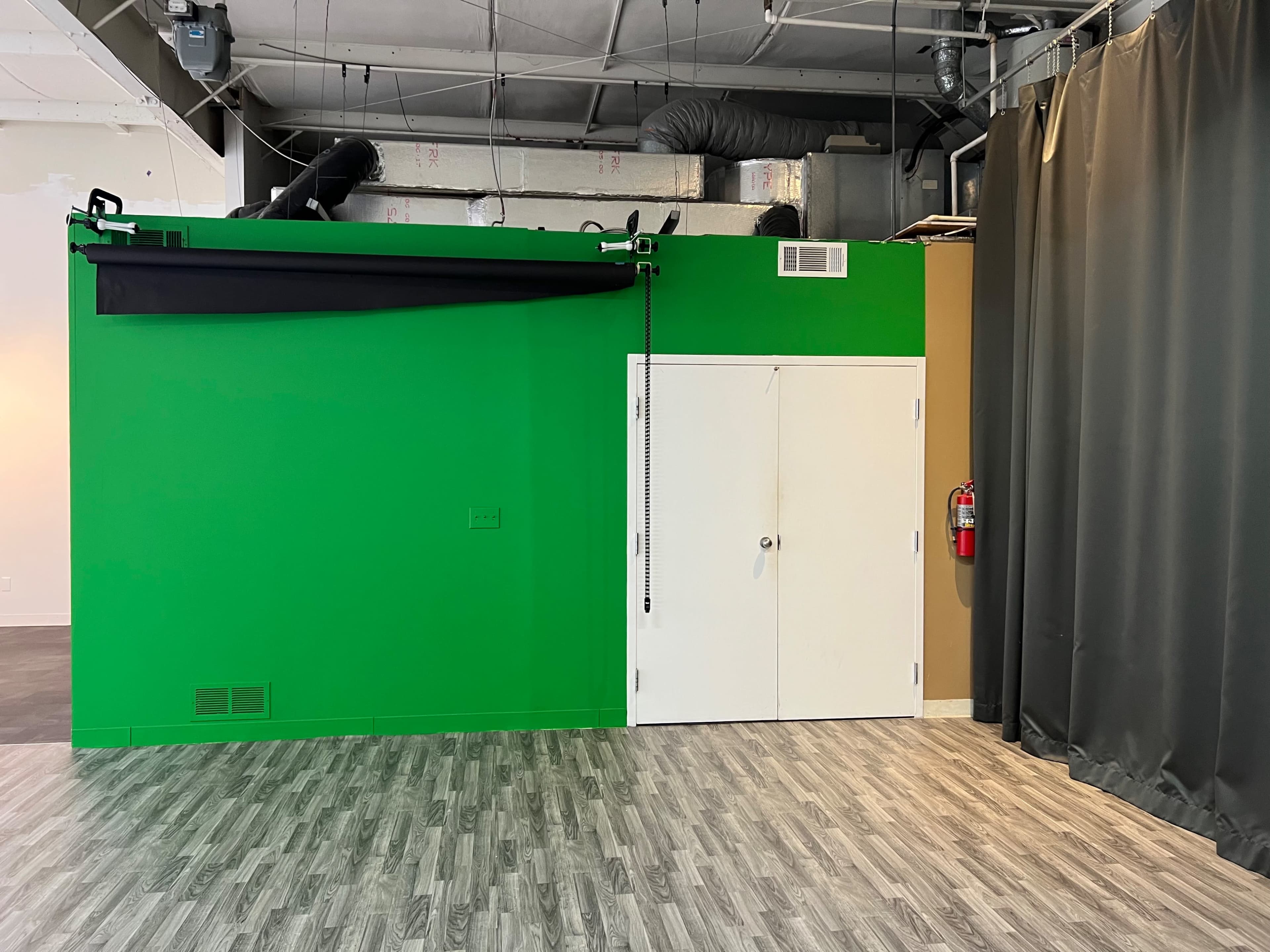 A room with a bright green wall, a door, and a curtain to the right, with a gray wooden floor.