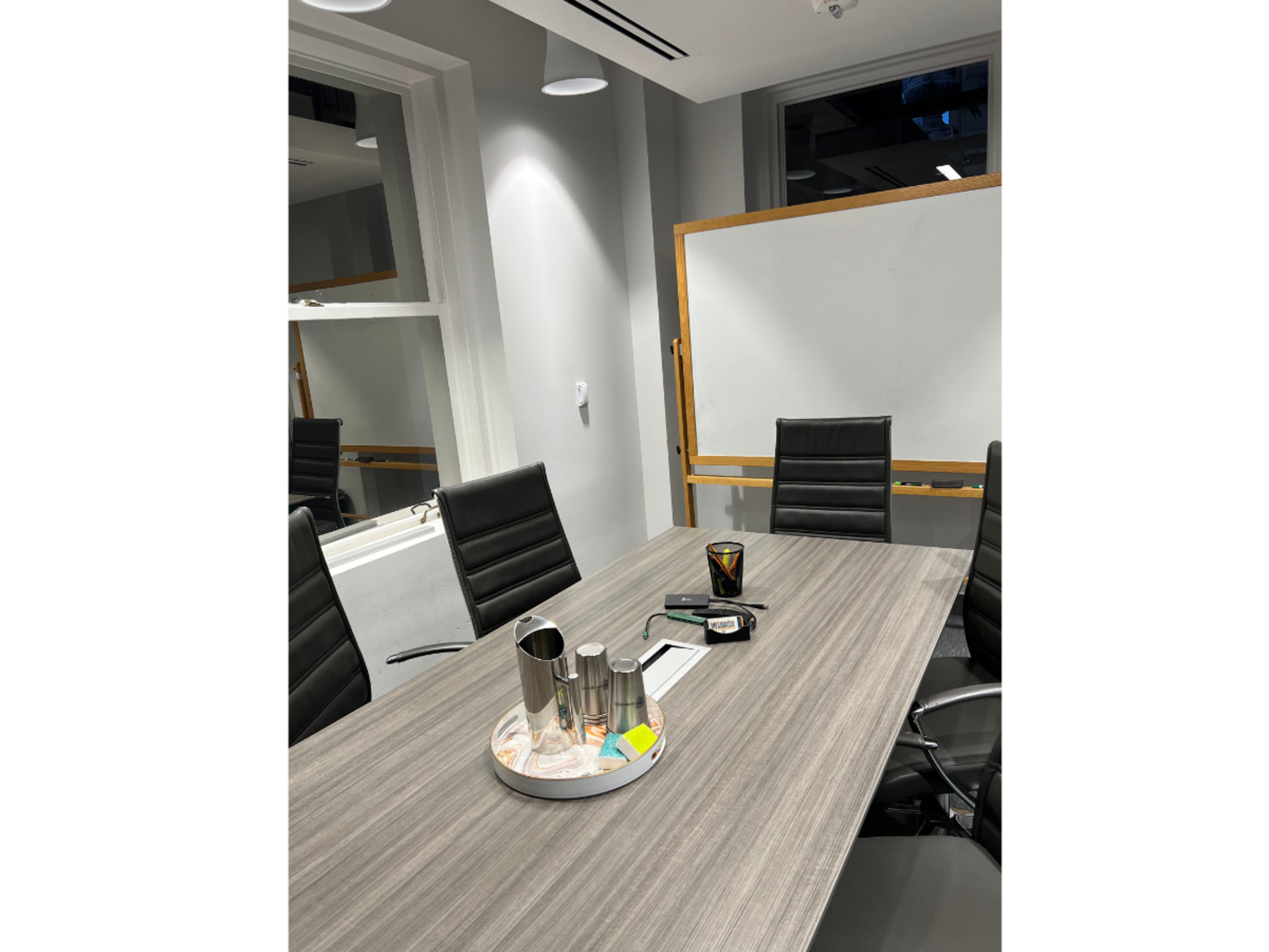 A modern conference room features a long wooden table, several black leather chairs, and a whiteboard in the background.