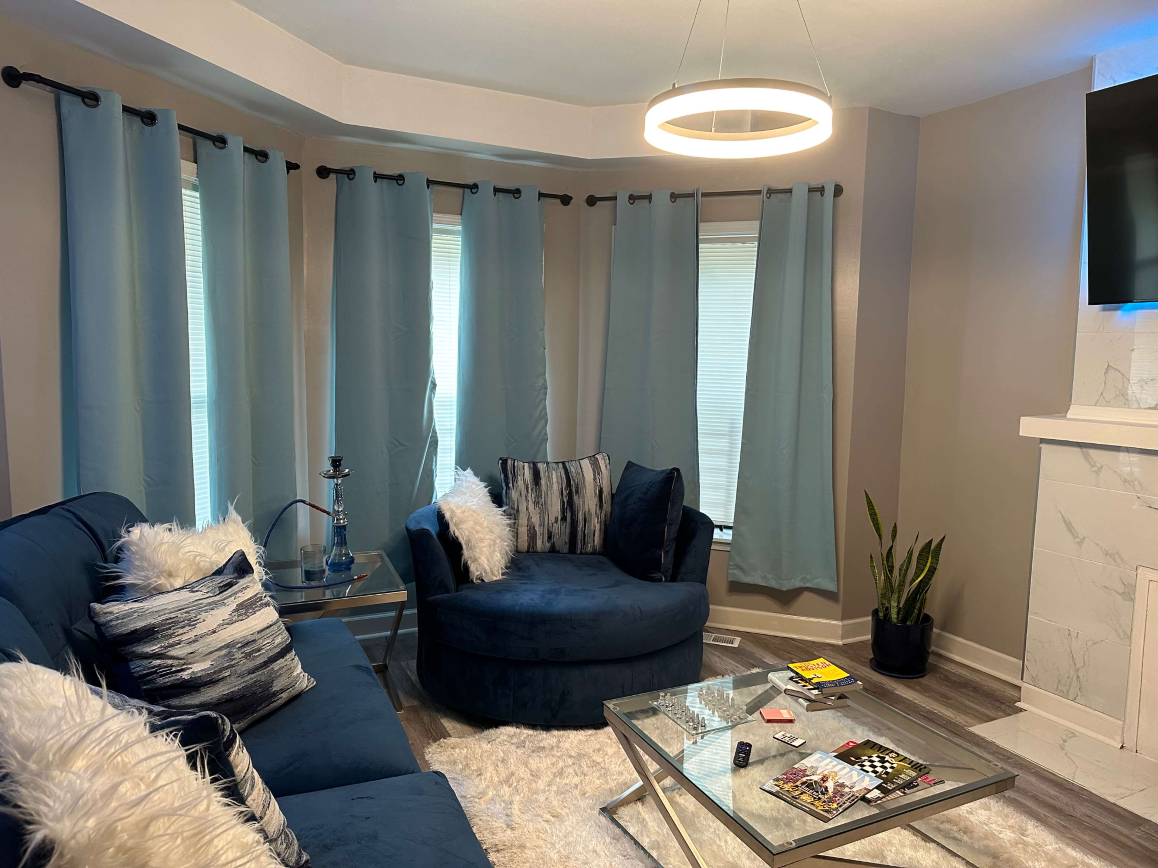 A living room with blue curtains, a round chair, a sectional sofa, a glass coffee table, and a white rug.