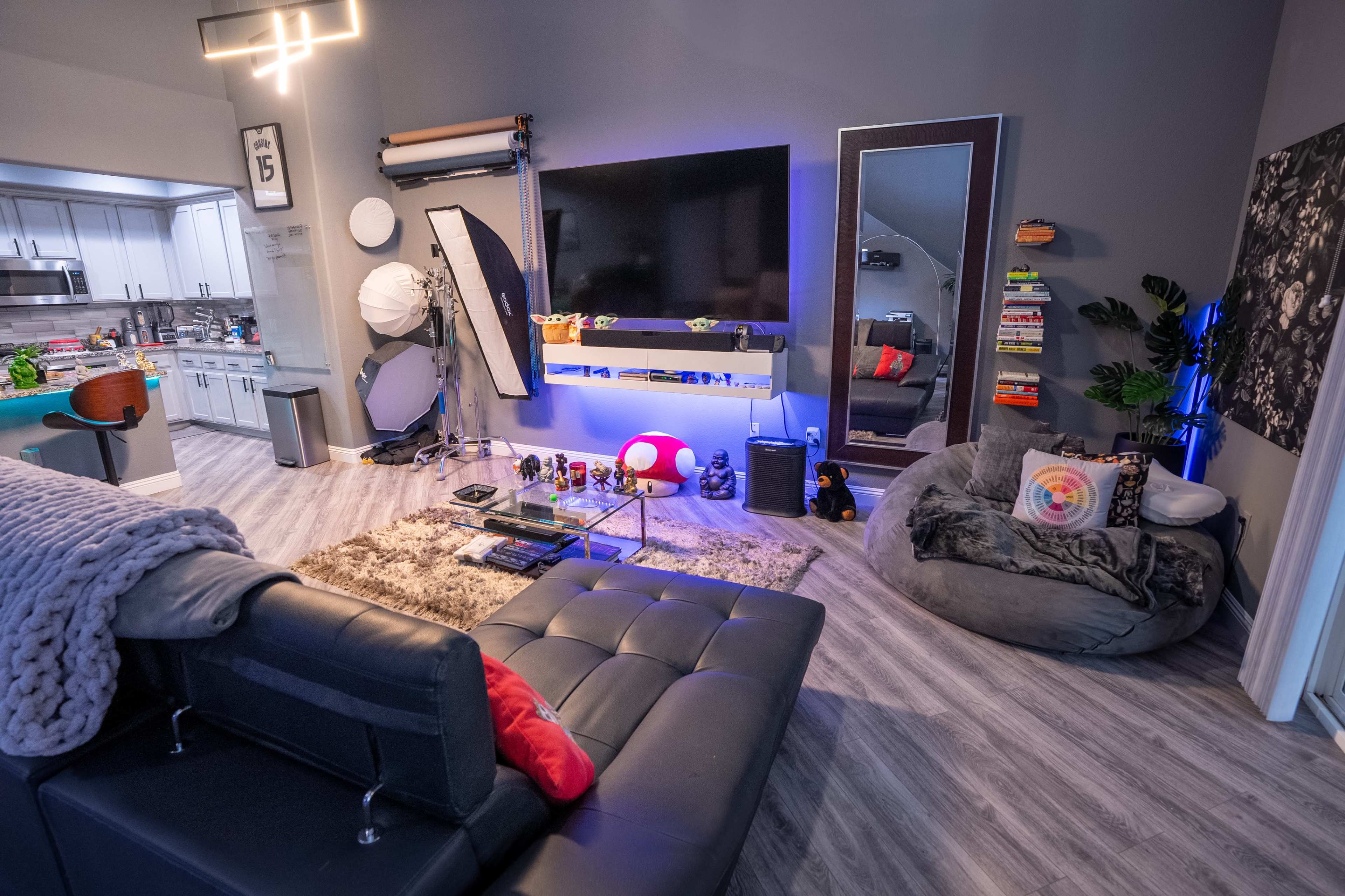 A modern living room featuring a sectional sofa, a large wall-mounted TV, a bean bag chair, and various decorative items on shelves against a gray wall.