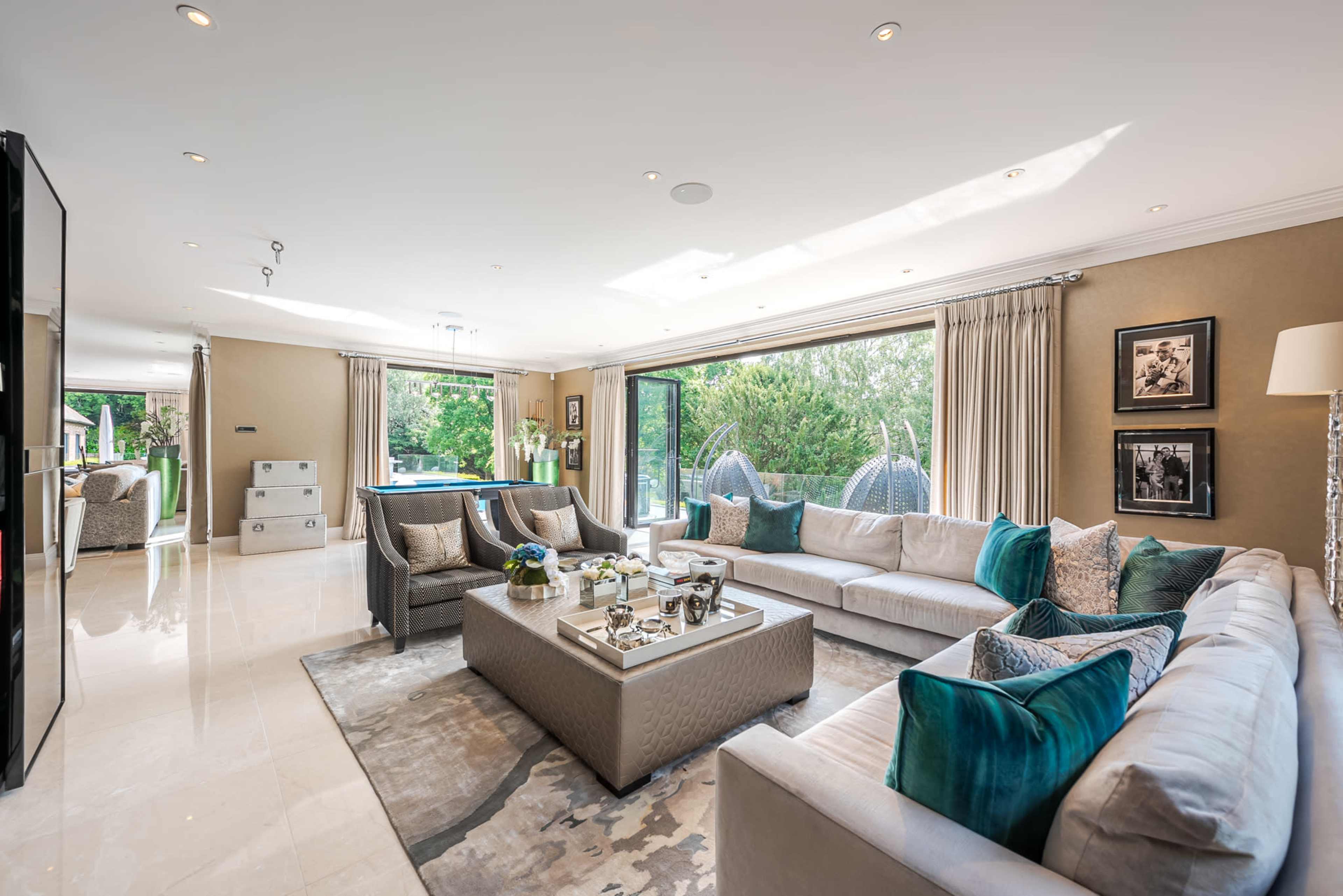 A spacious living room features large windows, plush sofas, and a contemporary arrangement with decorative cushions and a coffee table.
