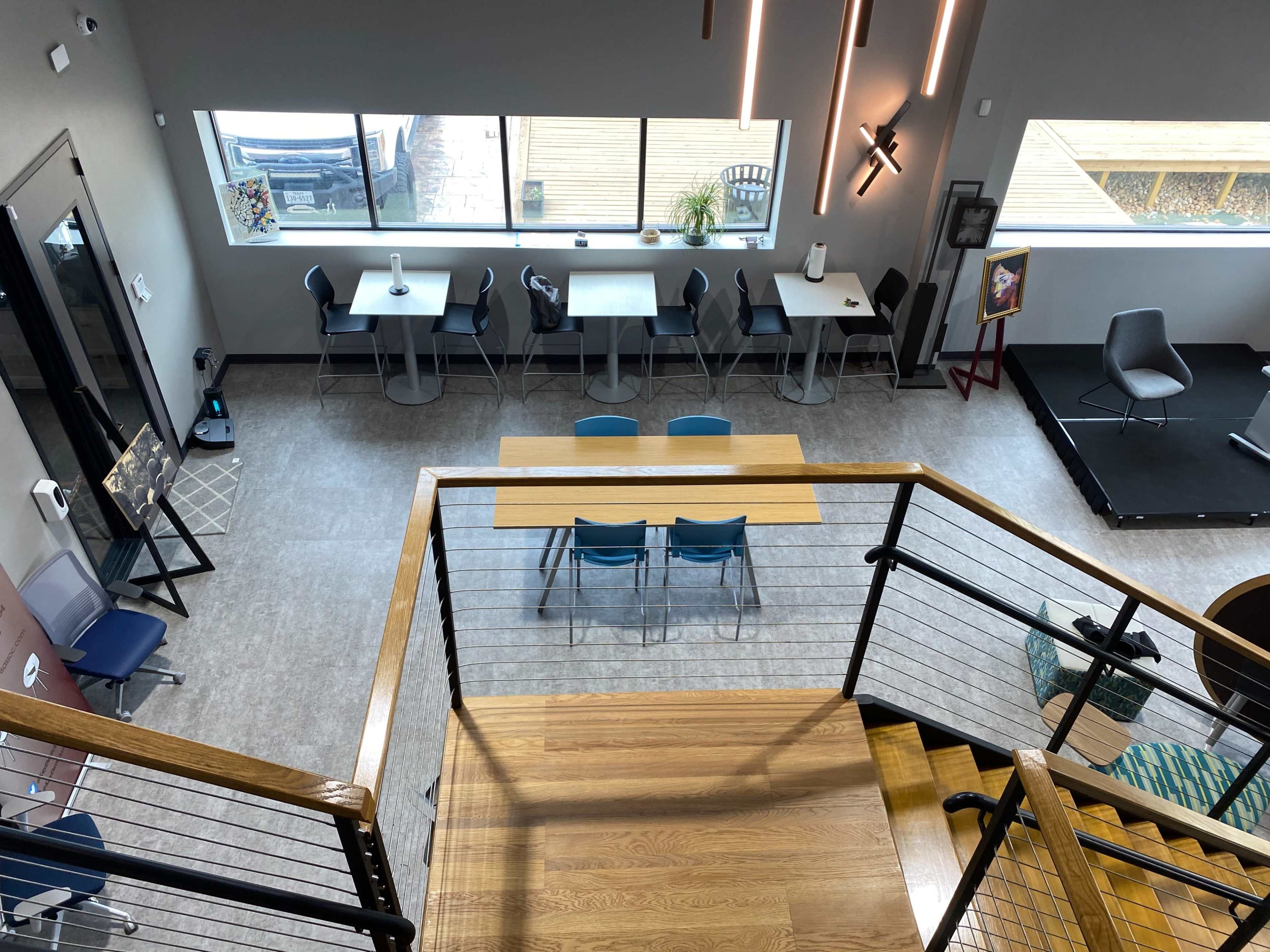 The image shows a modern multi-level workspace featuring tables, chairs, and large windows that provide natural light.