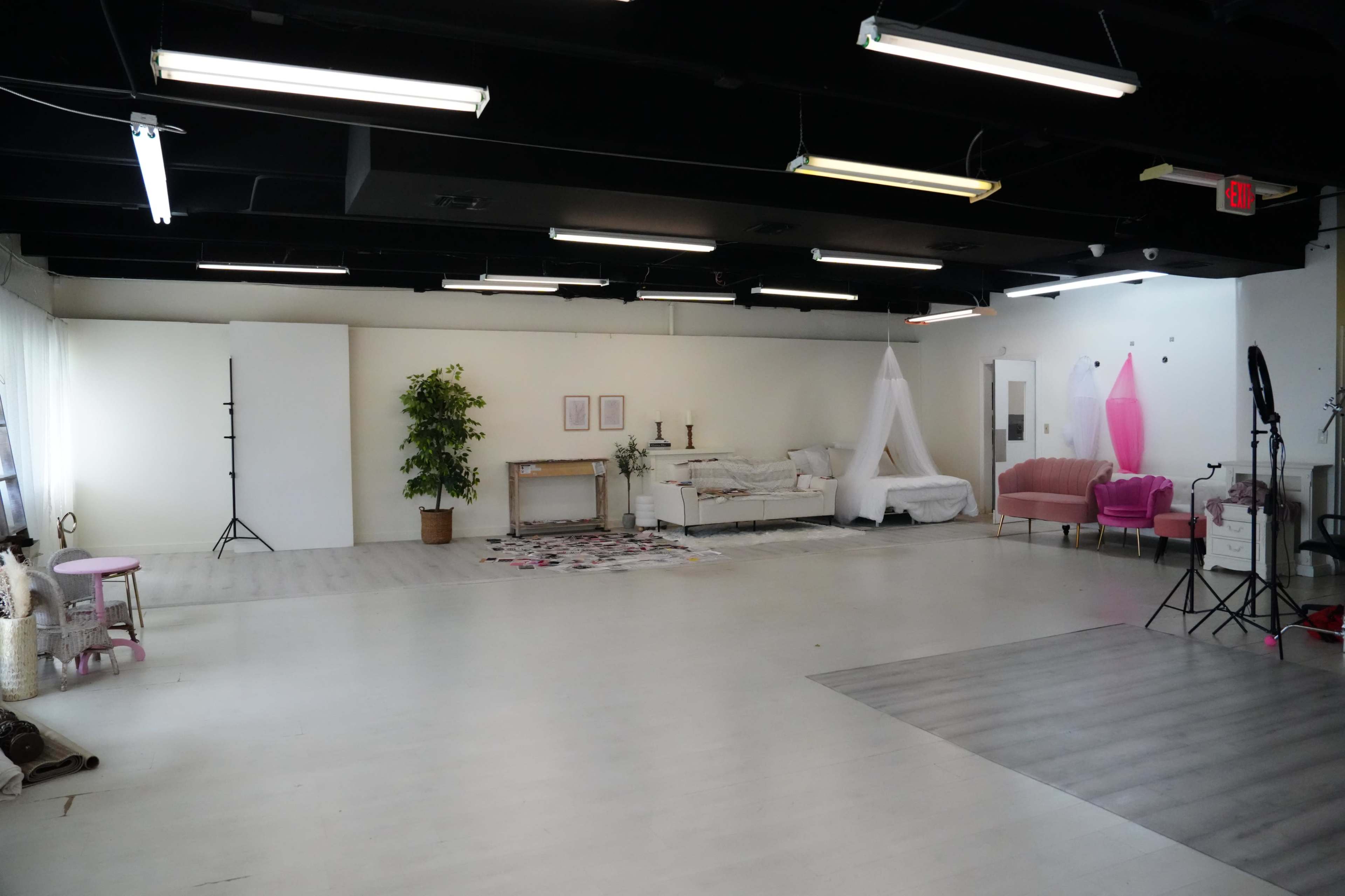 A spacious studio interior with a bed, a pink sofa, and various lighting equipment.