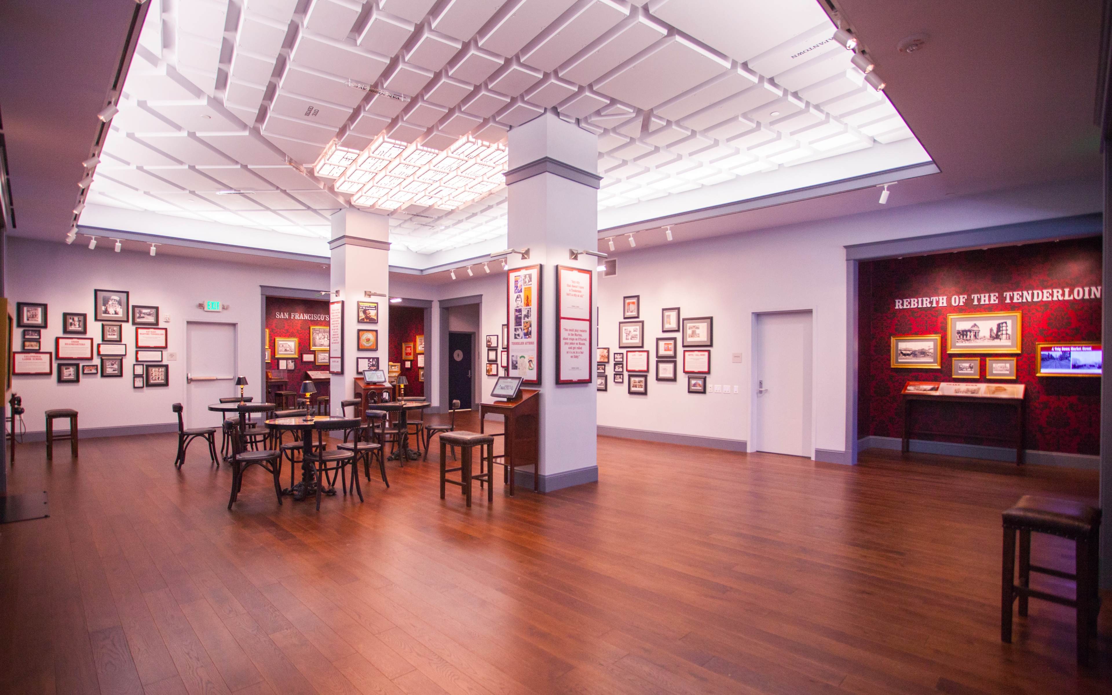 A spacious gallery with wooden floors, displaying framed photographs and information panels on the walls.