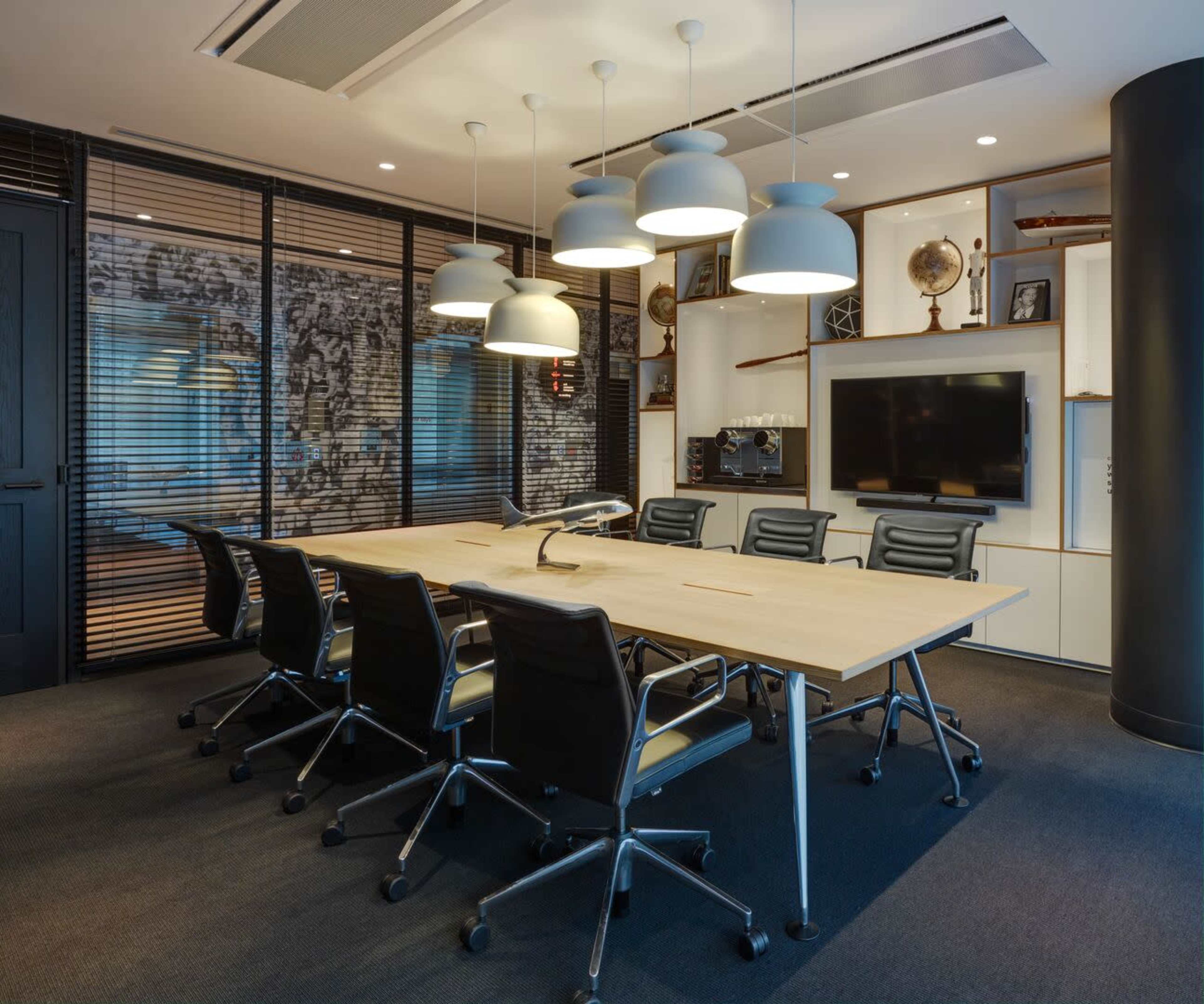 A modern conference room features a large table surrounded by black chairs, with pendant lights overhead and a wall adorned with framed artwork.