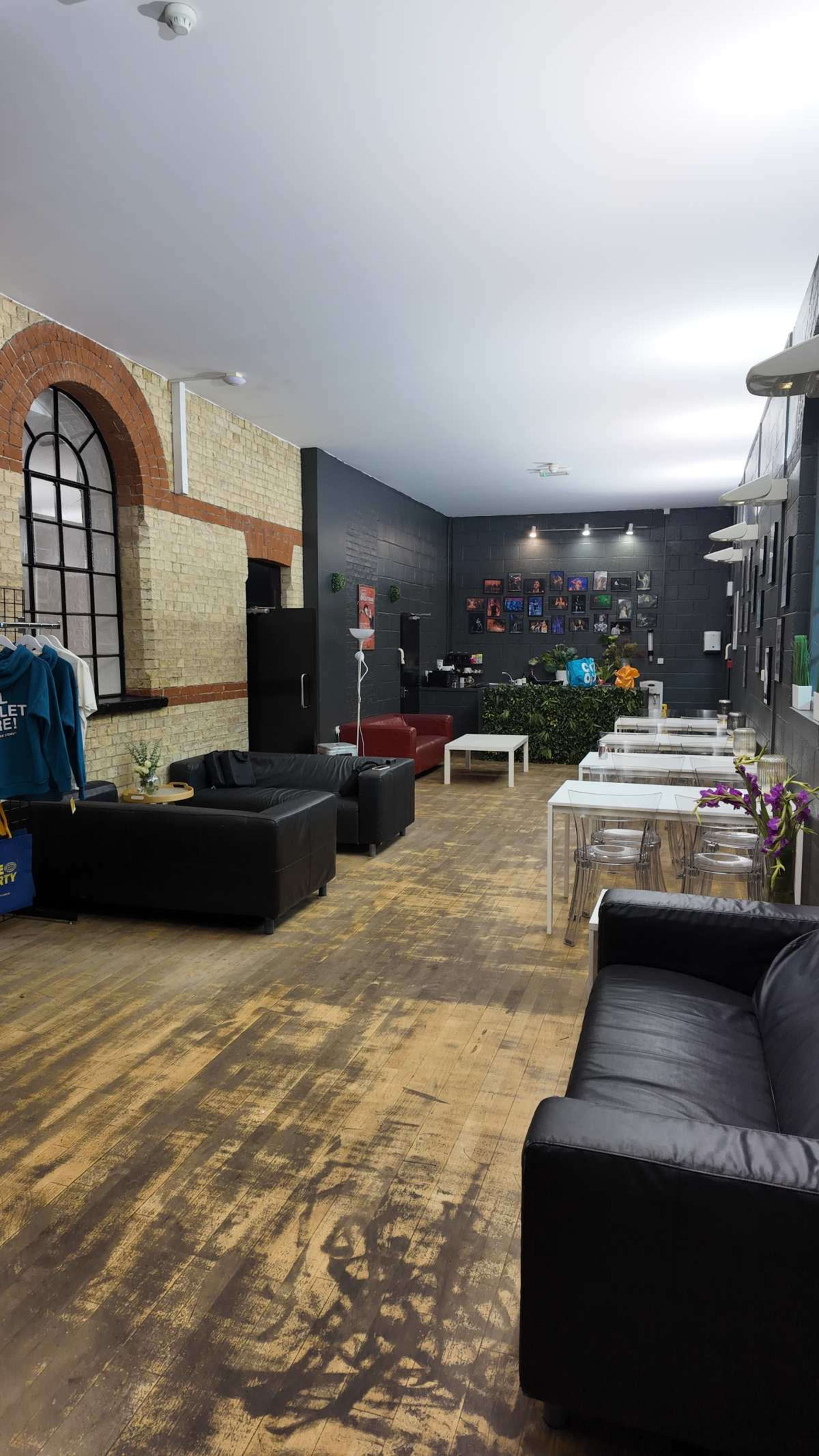 The image shows a spacious indoor area featuring black leather sofas, tables, and various decorations on the walls, with a mix of seating arrangements and plants.