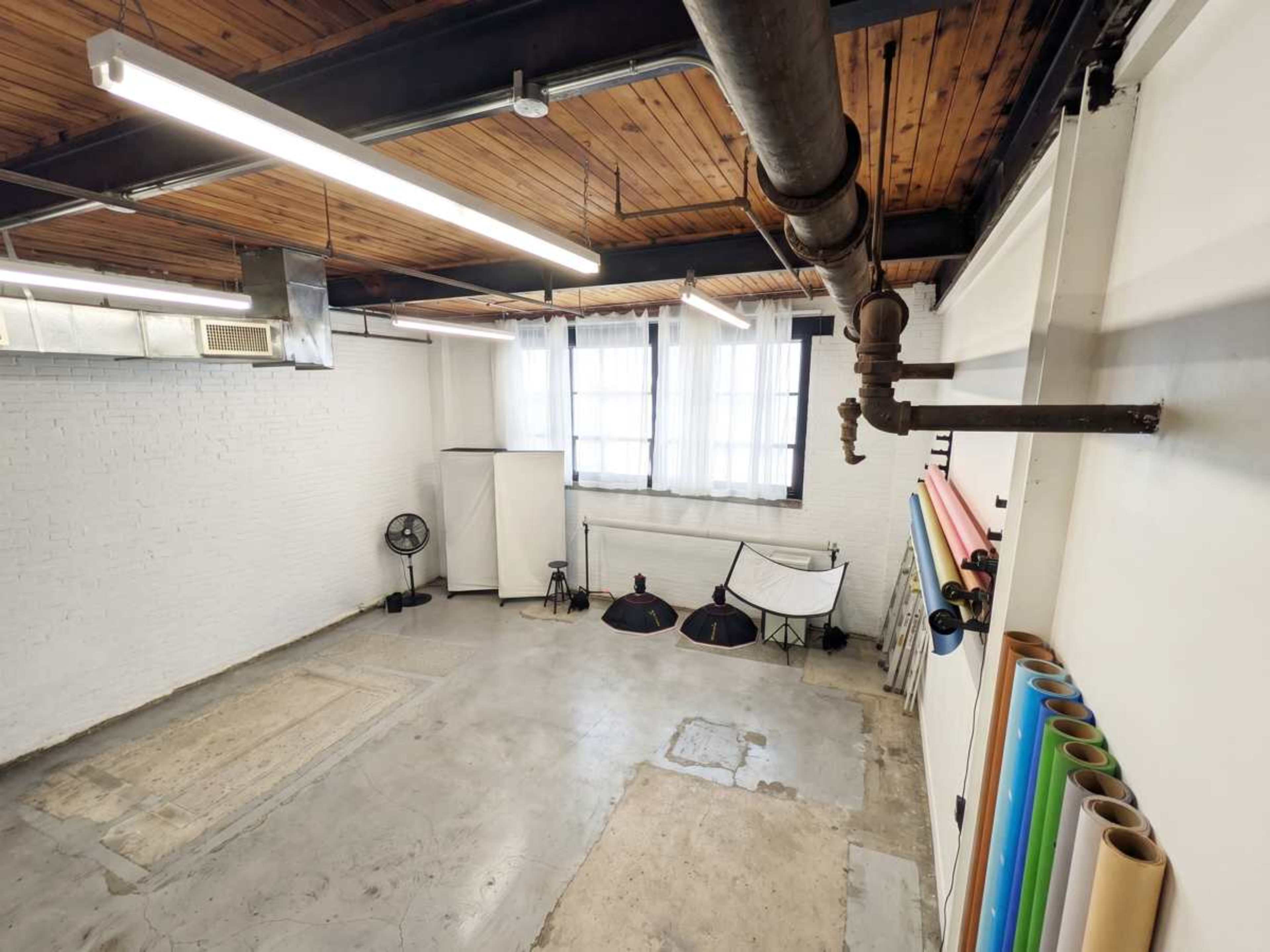 The image shows a spacious studio with concrete flooring, large windows, and photography equipment such as softbox lights and backdrops.