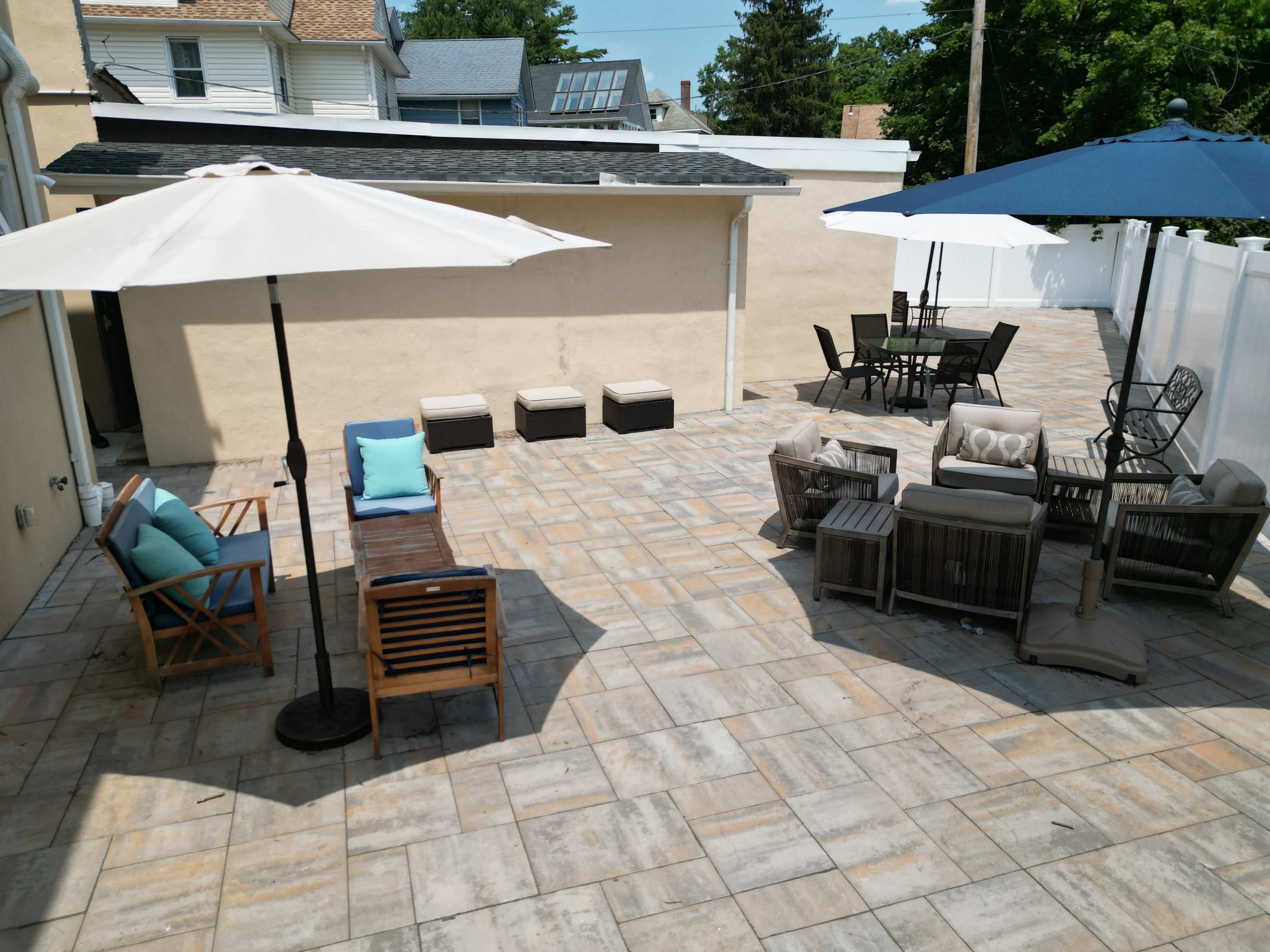 The image shows a patio area featuring several seating arrangements, including lounge chairs, a dining table, and umbrellas for shade.