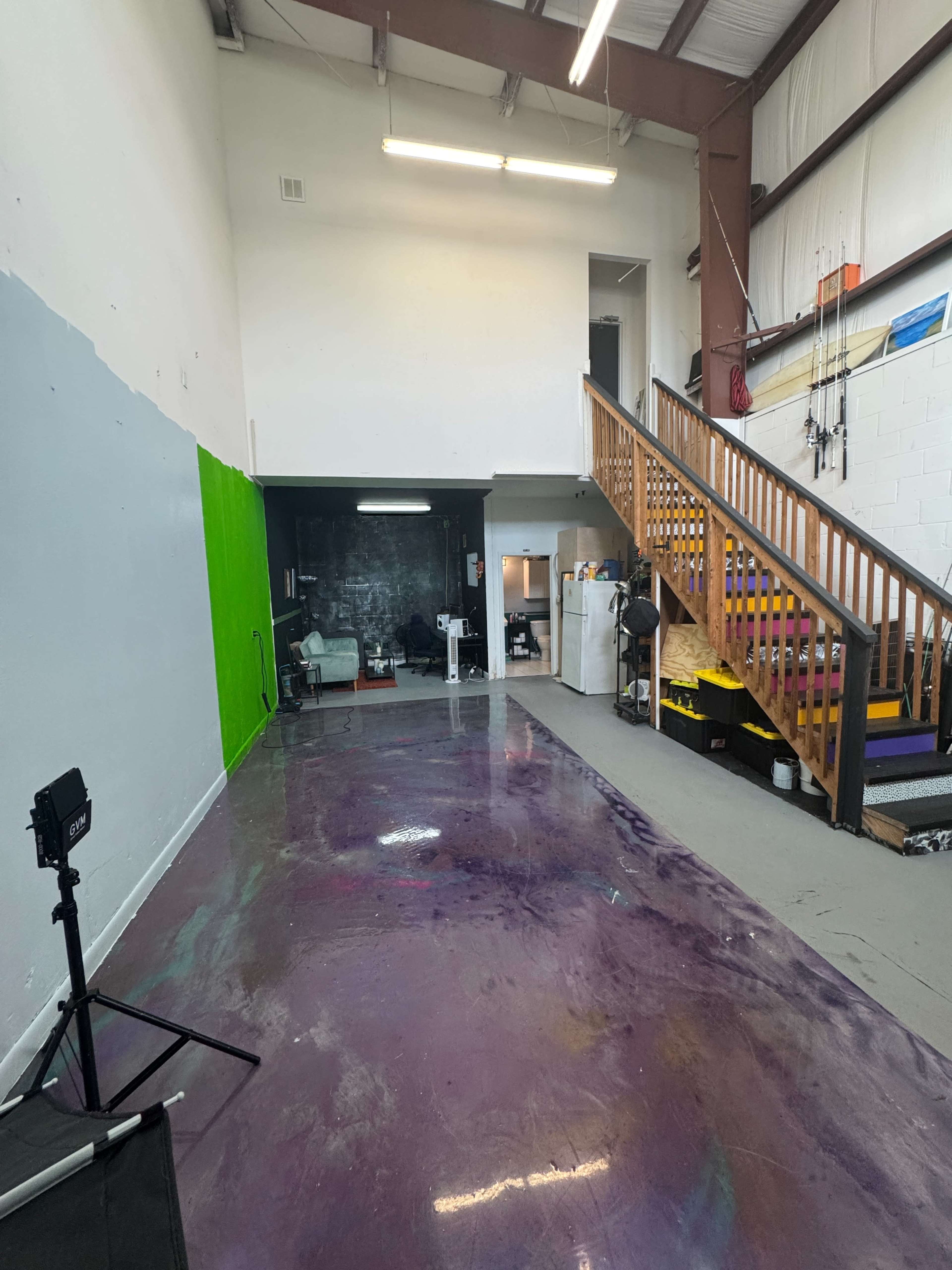 The image depicts a spacious room with a purple-painted floor, a green screen wall on one side, and a staircase leading to an upper level.
