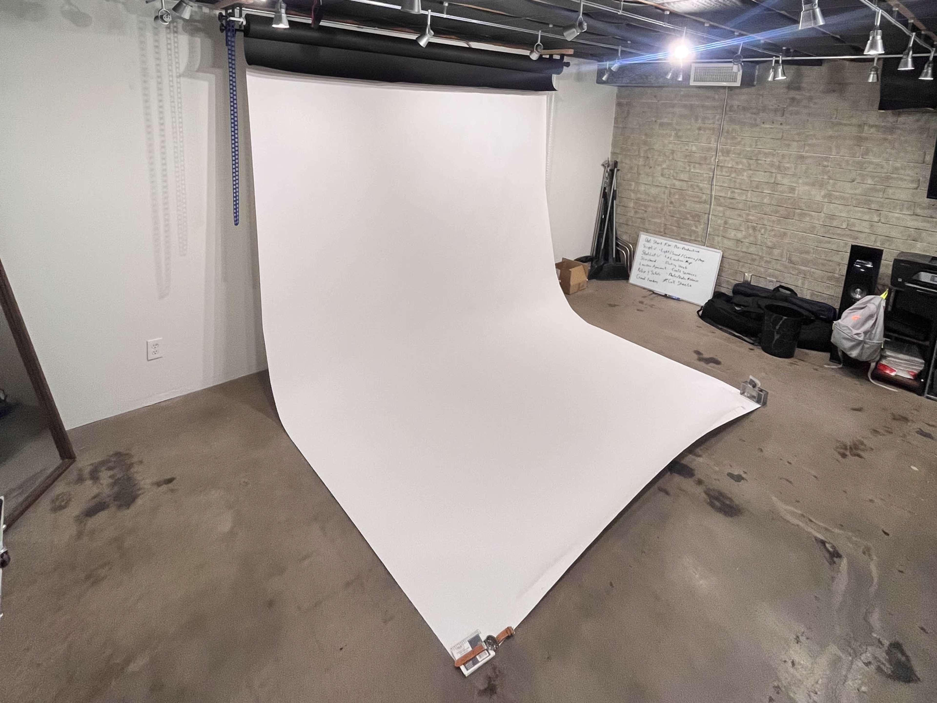 A smooth, white backdrop is set up in a dimly lit room with concrete flooring and various equipment in the background.