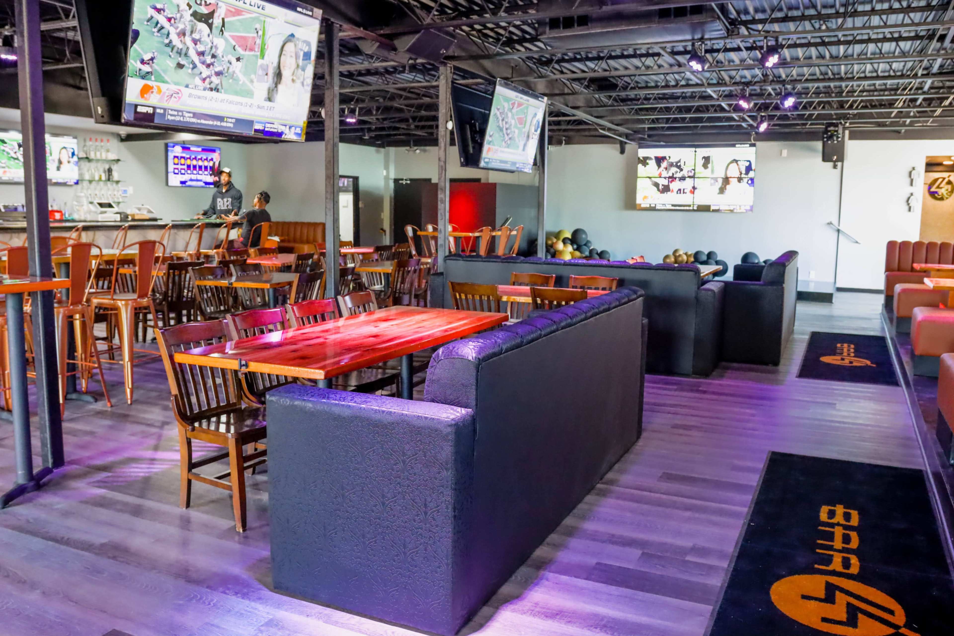 A sports bar with seating areas, tables, and multiple screens displaying games.
