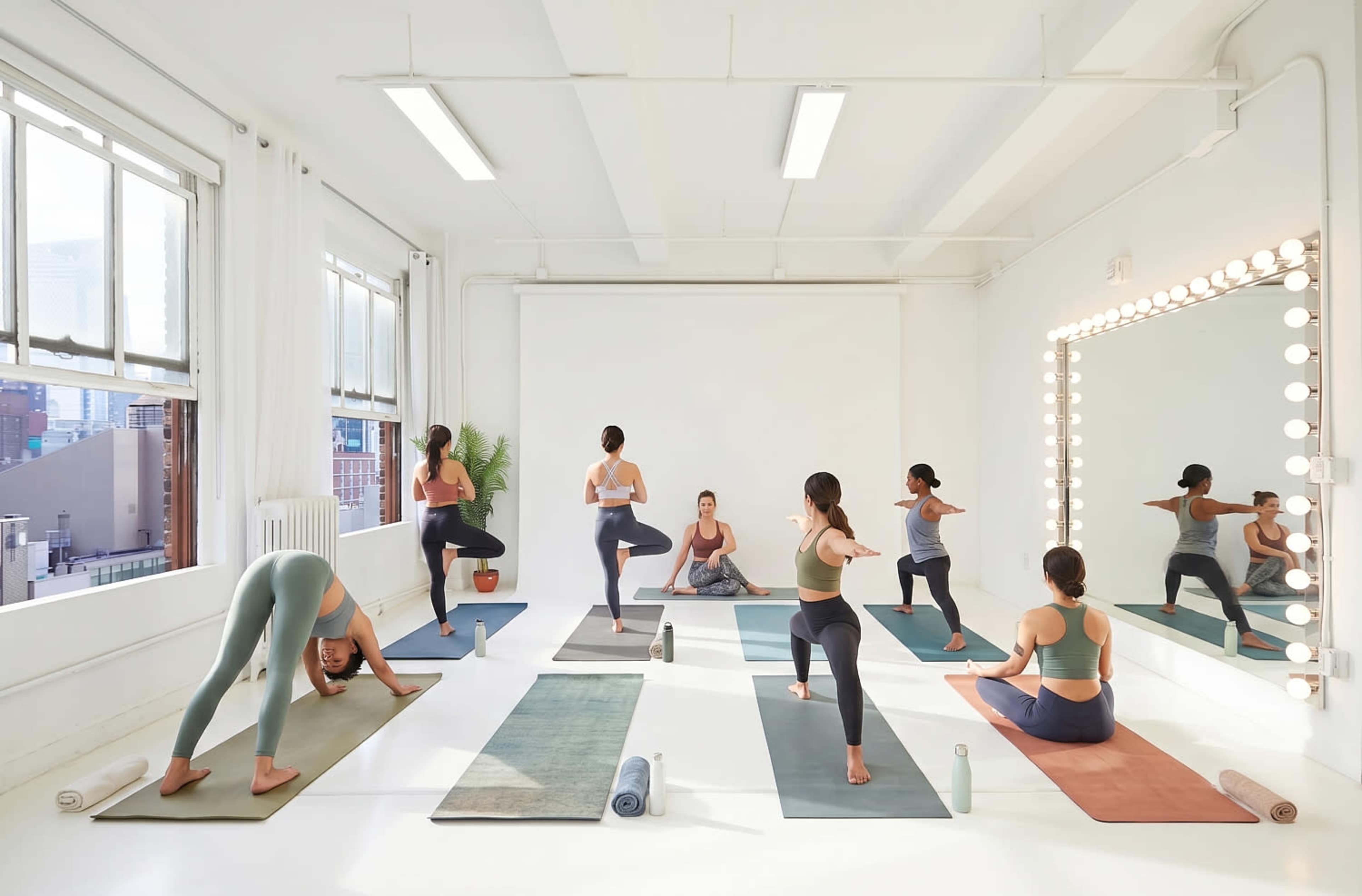 A group of individuals is practicing yoga in a spacious, well-lit studio with large windows and mirrors.