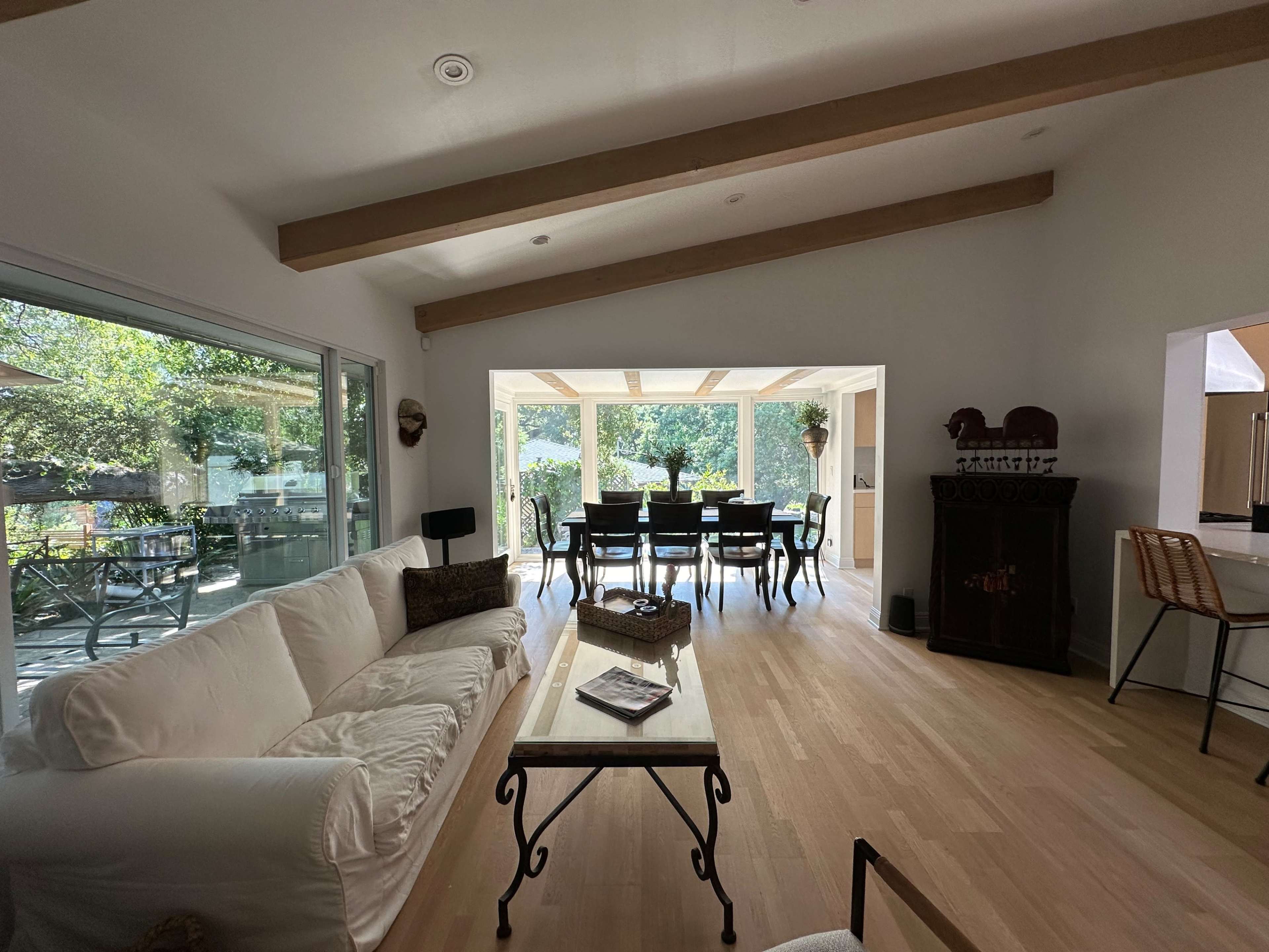 A modern living room with a white sofa, a coffee table, and a view of a dining area through large glass doors overlooking an outdoor space.