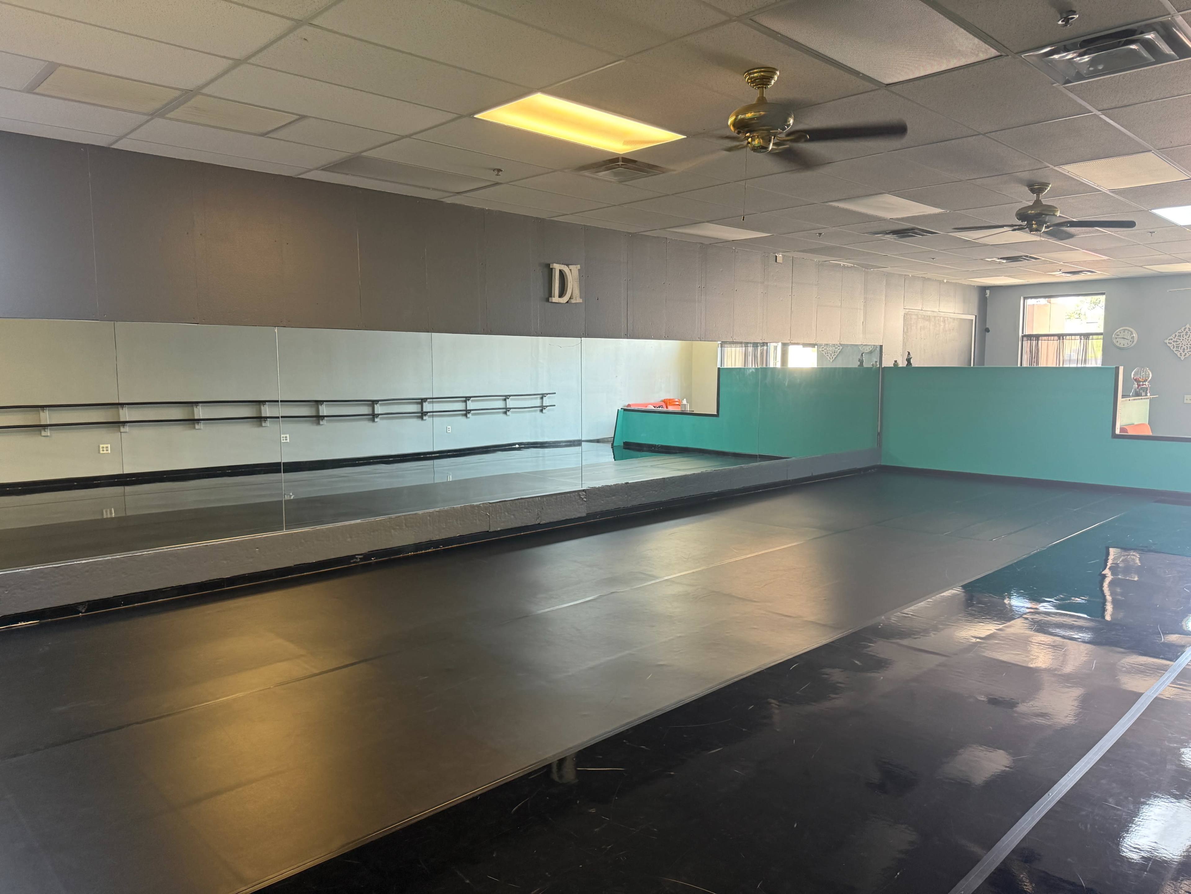 The image shows a dance studio with a black floor, mirrors on one wall, and a teal accent wall.