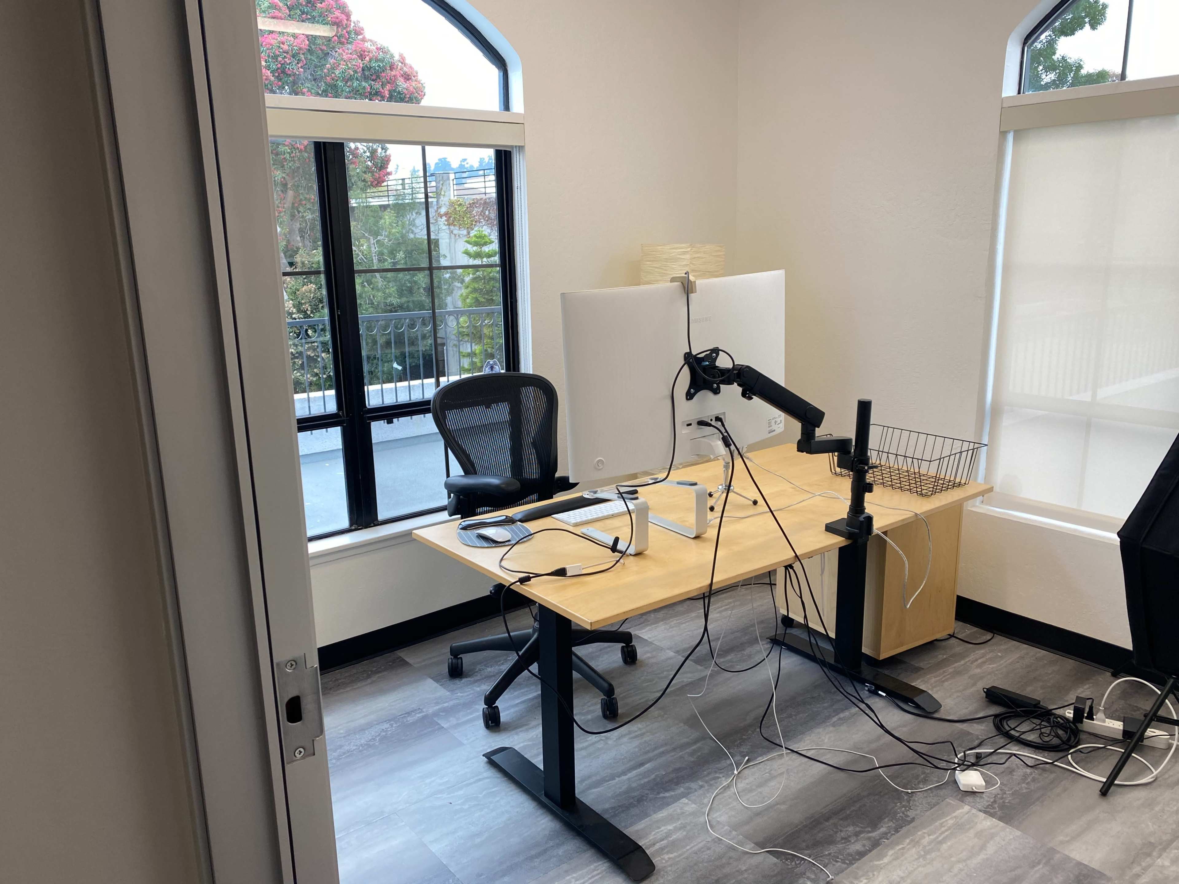 A workspace with a desk, a monitor mounted on an arm, a chair, and various cables resting on the floor.
