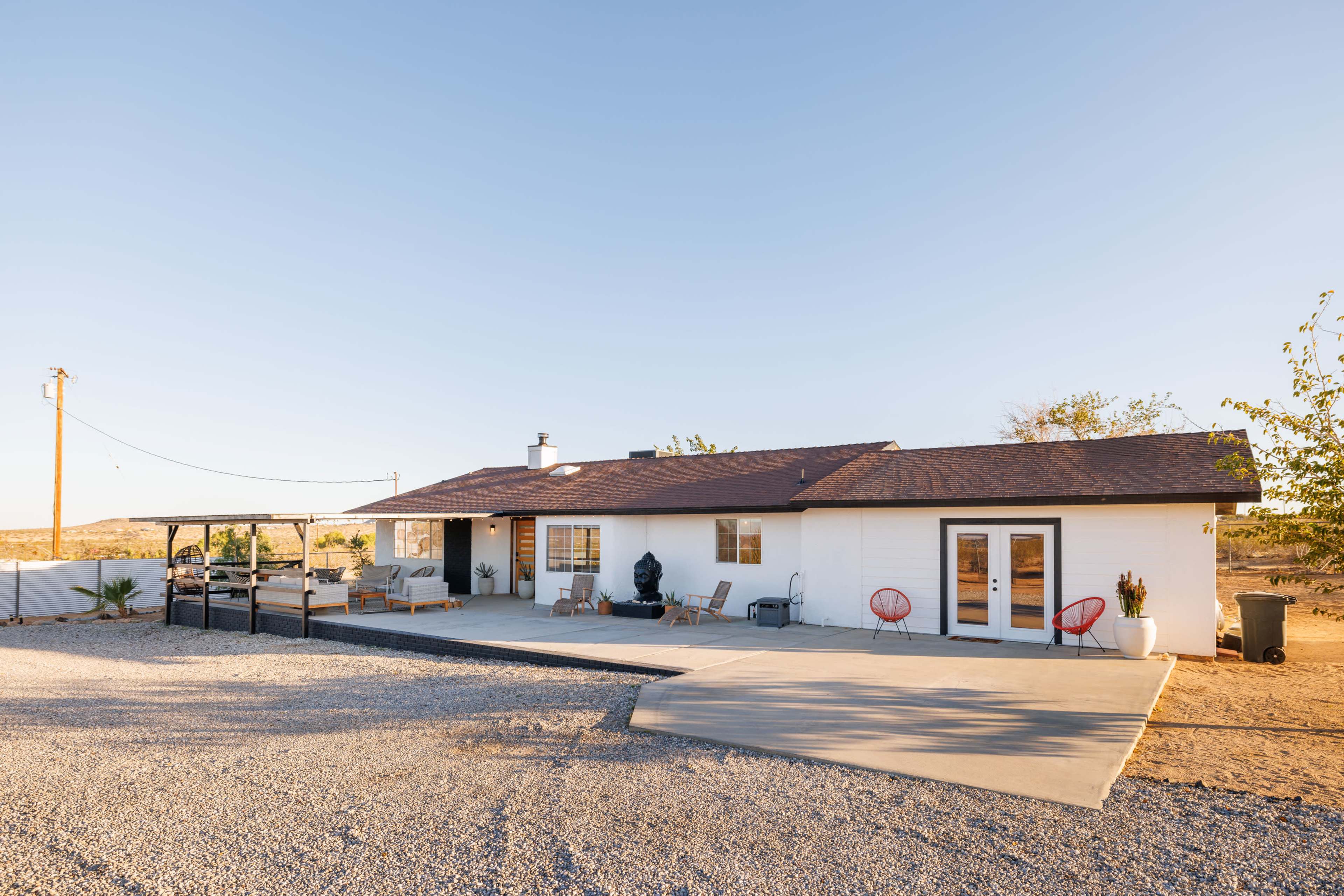 A single-story house with a patio and gravel driveway is set against a clear sky in a desert landscape.