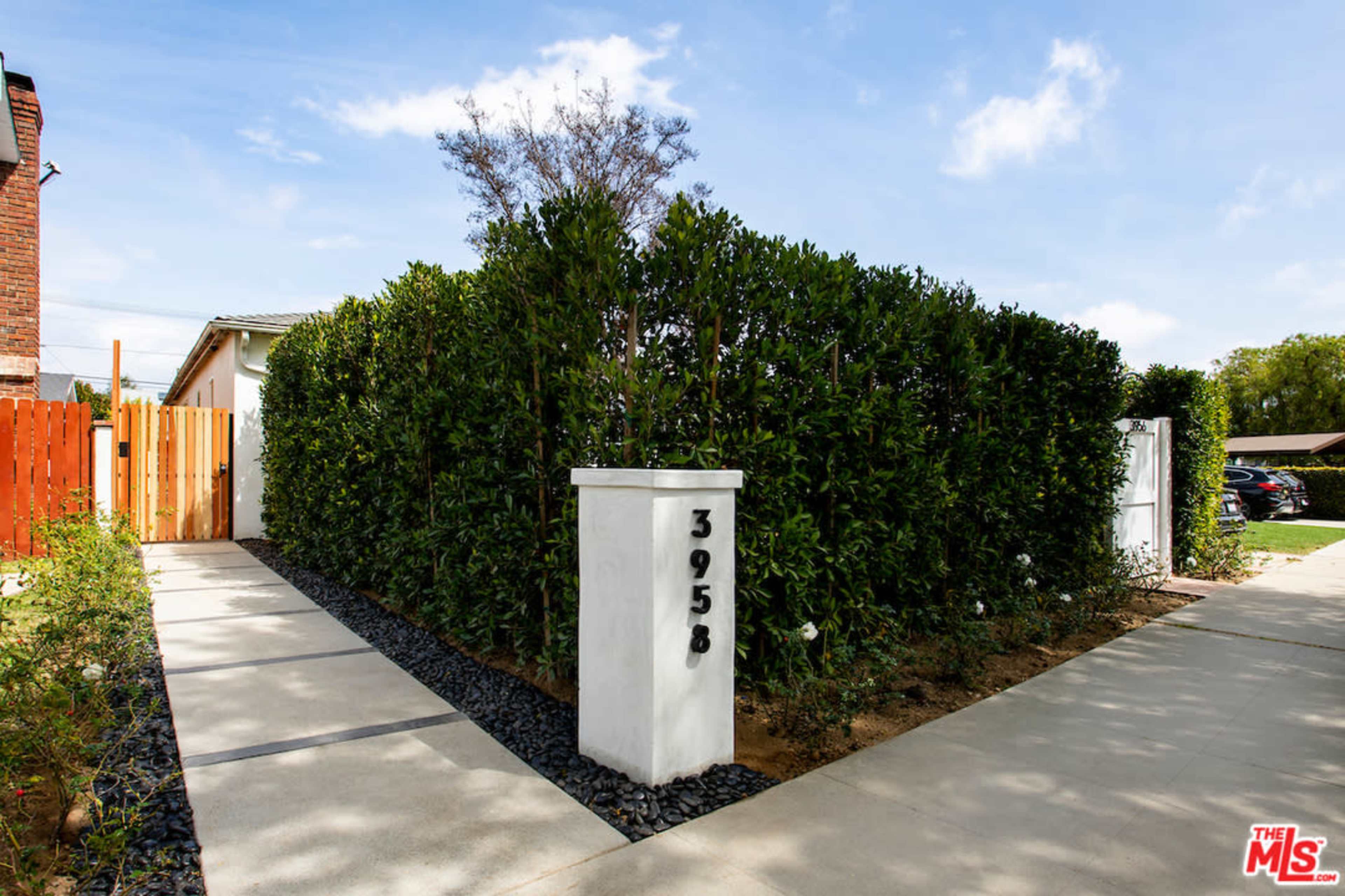 A white pillar marked with the number 3958 stands at the entrance of a pathway surrounded by tall green hedges.