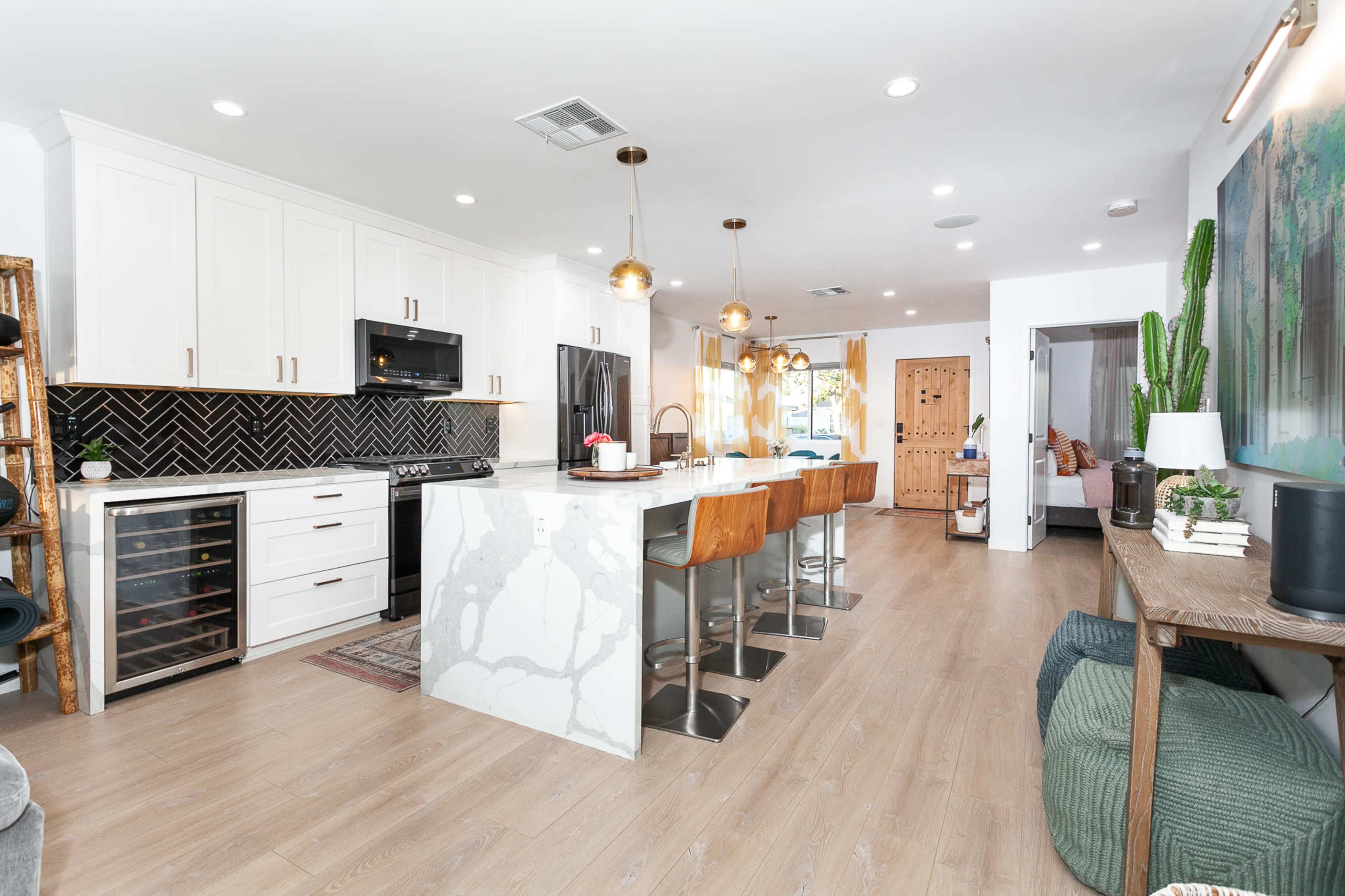 A modern kitchen features a marble island with bar stools, white cabinets, and a tile backsplash.