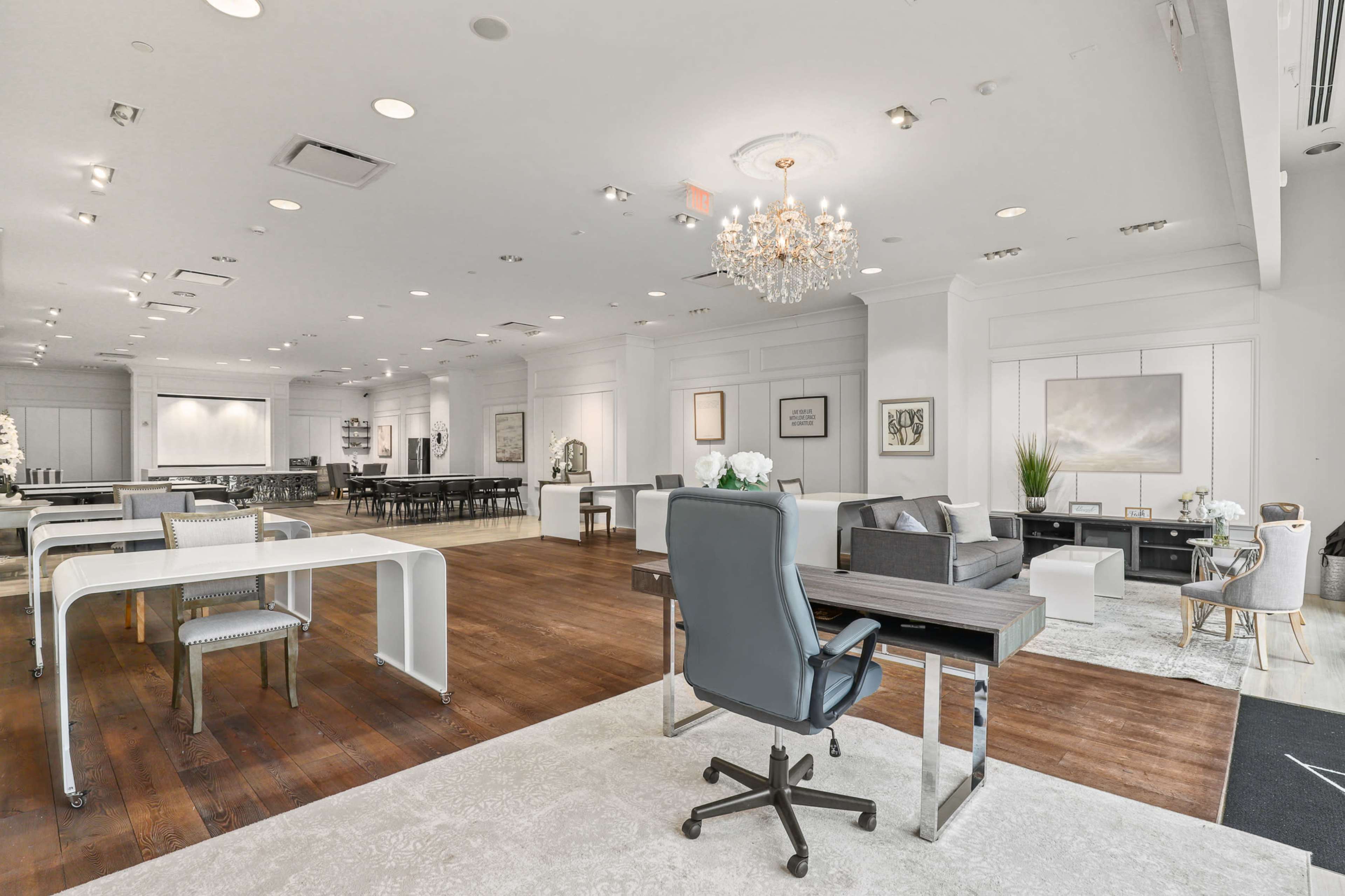 The image shows a spacious, modern office interior featuring a mix of workstations, seating areas, and decorative elements with a chandelier overhead.