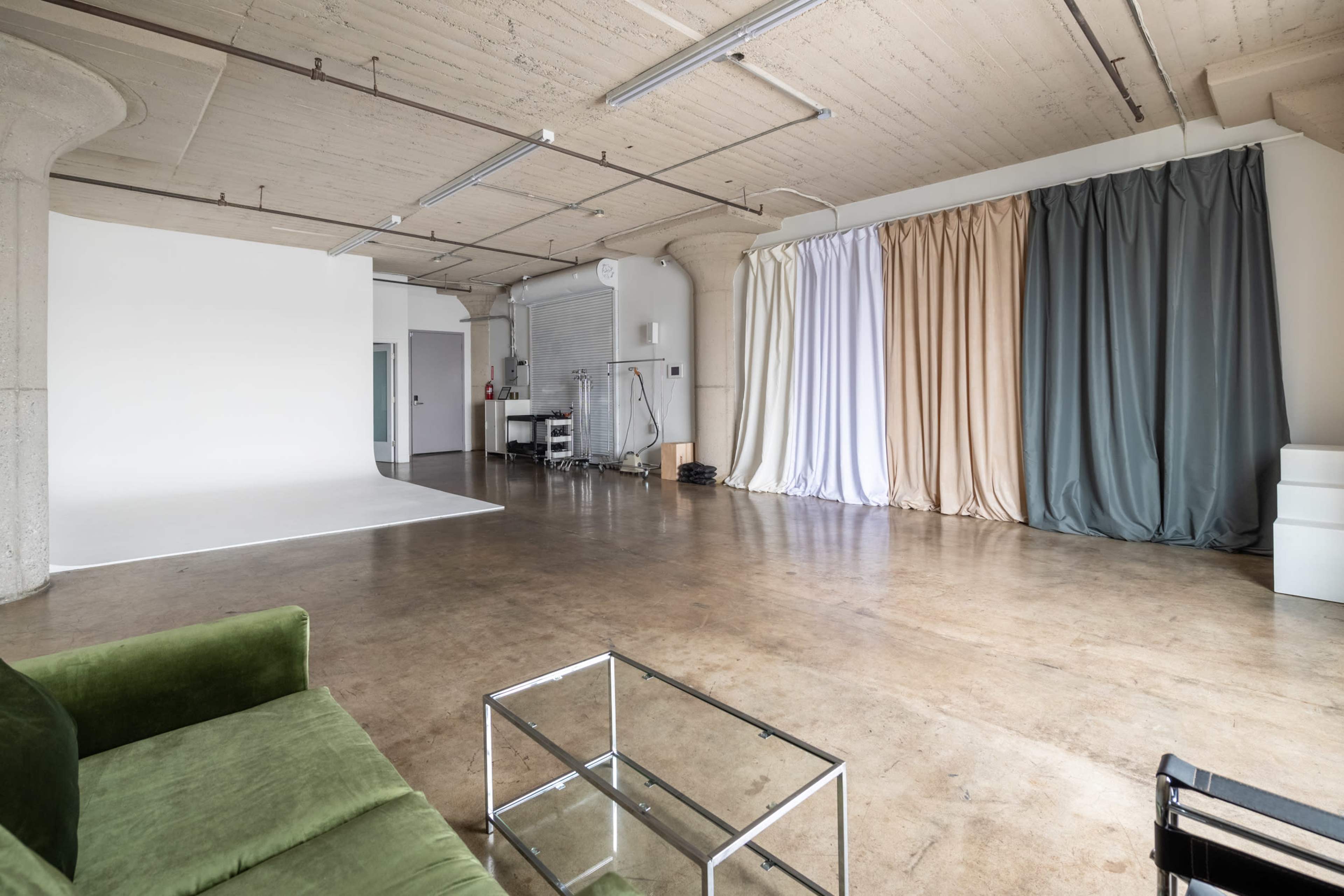 The image shows a spacious, empty studio with a concrete floor, a white backdrop, and draped fabric in muted colors along one wall.