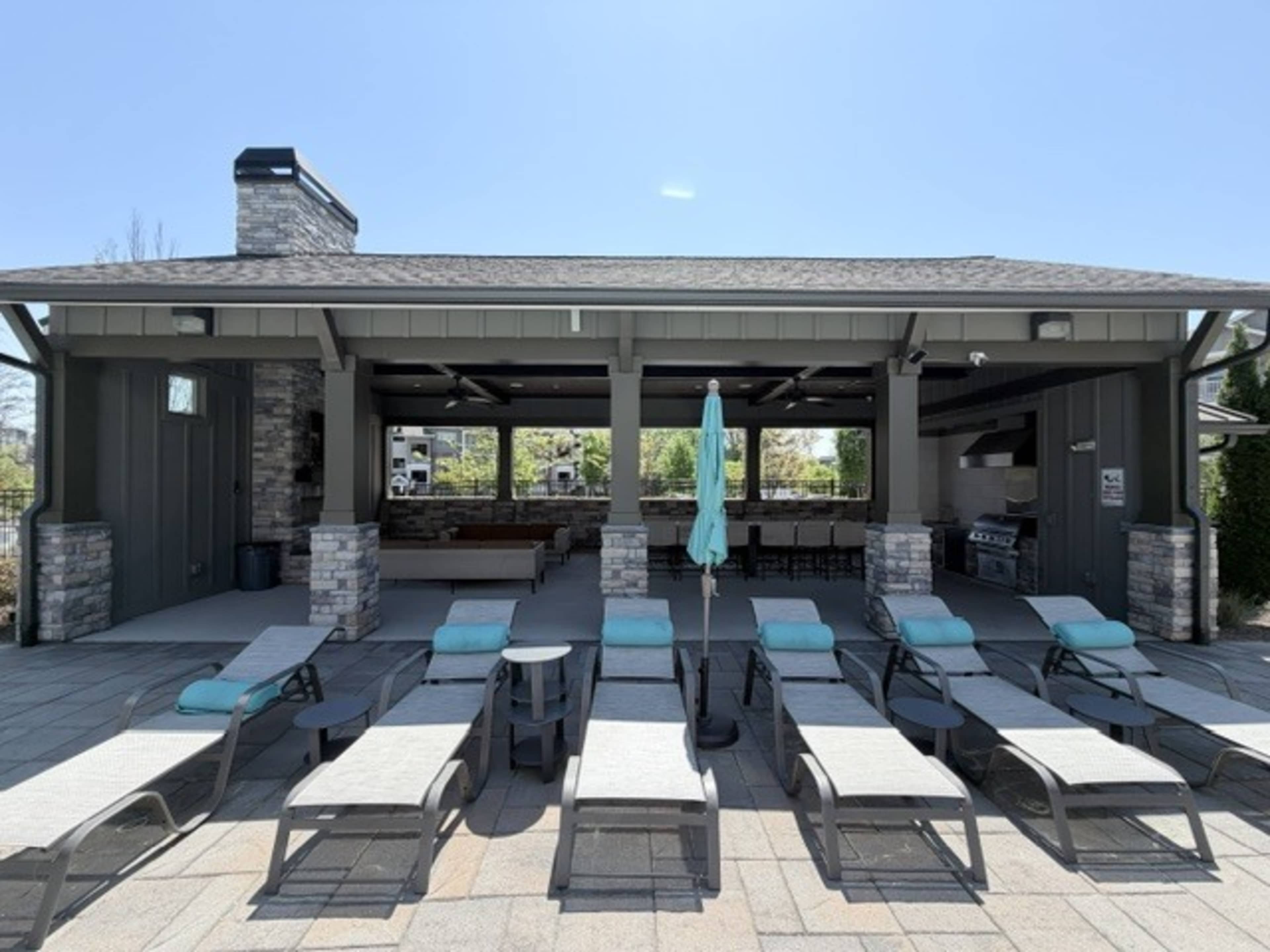 The image shows a poolside cabana area with several loungers and a barbecue station under a covered structure.