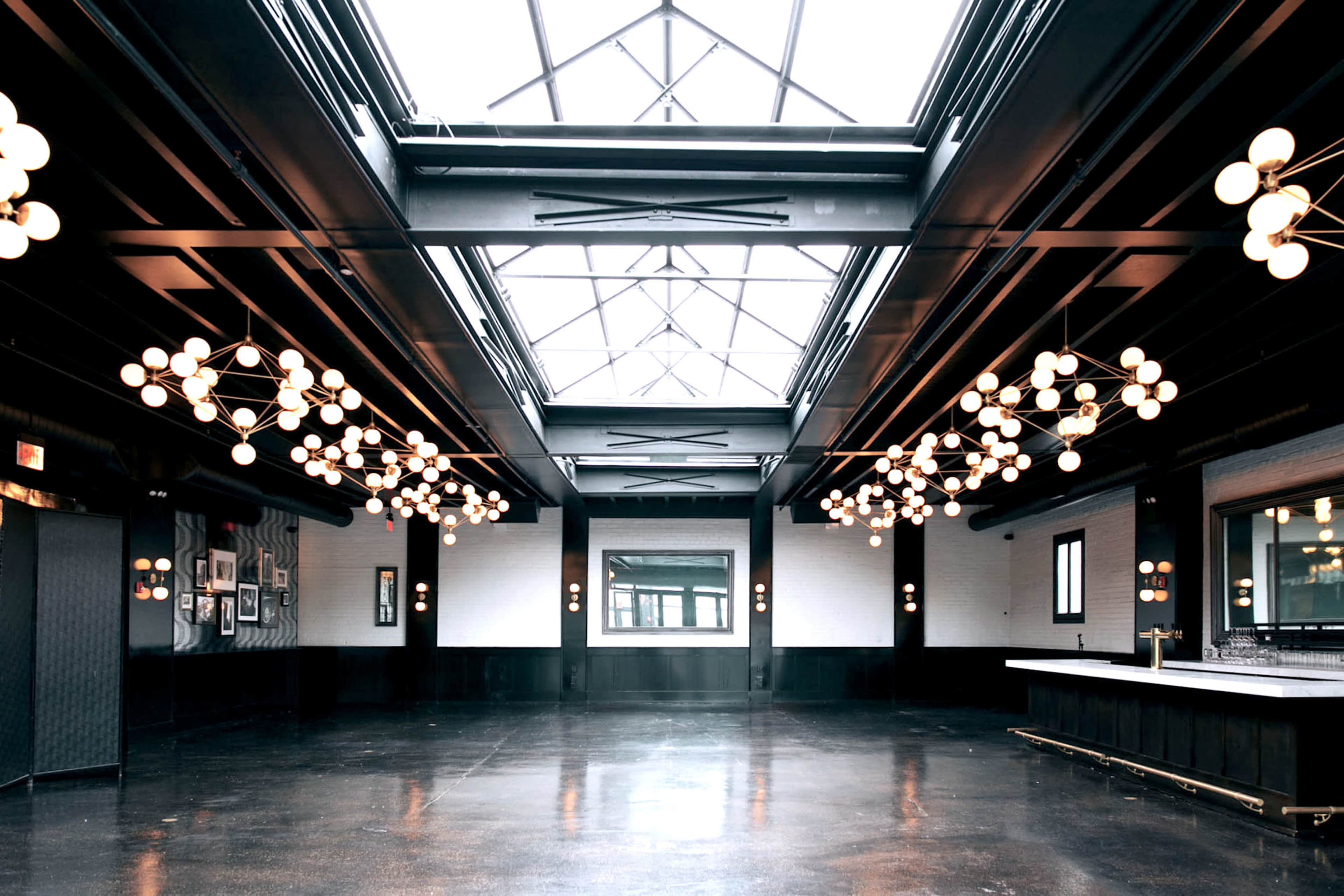 A spacious, modern interior with large windows, a high ceiling, and numerous decorative light fixtures.